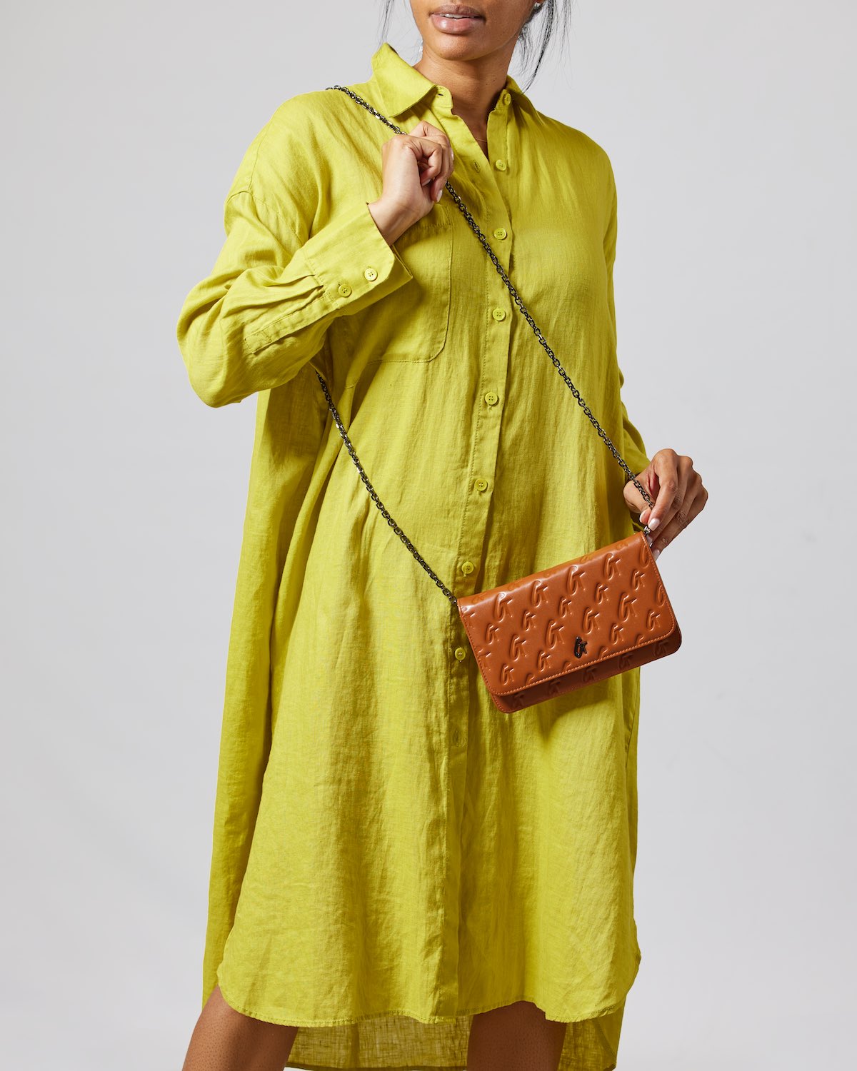 Monogram gunmetal and brown WOC handbag with embossed logo pattern, worn with a yellow shirt dress.