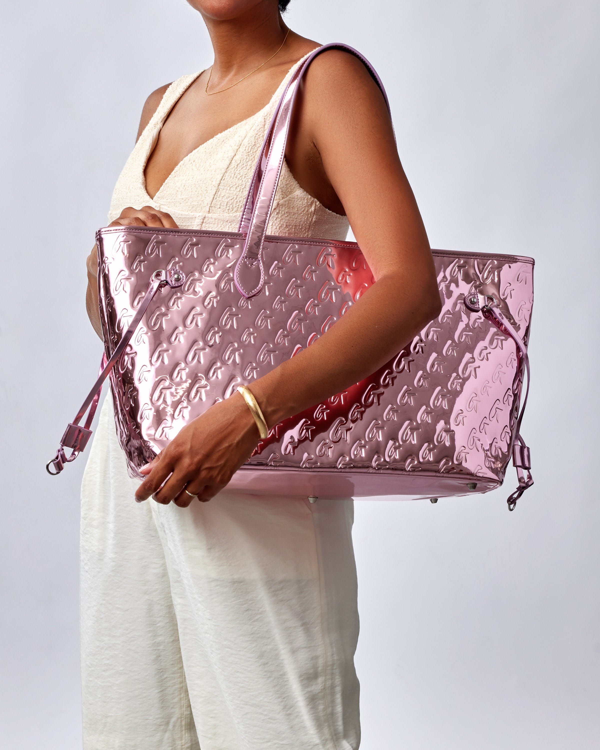 A person holding a metallic pink tote bag featuring a monogram design, showcasing its shiny surface and spacious interior.
