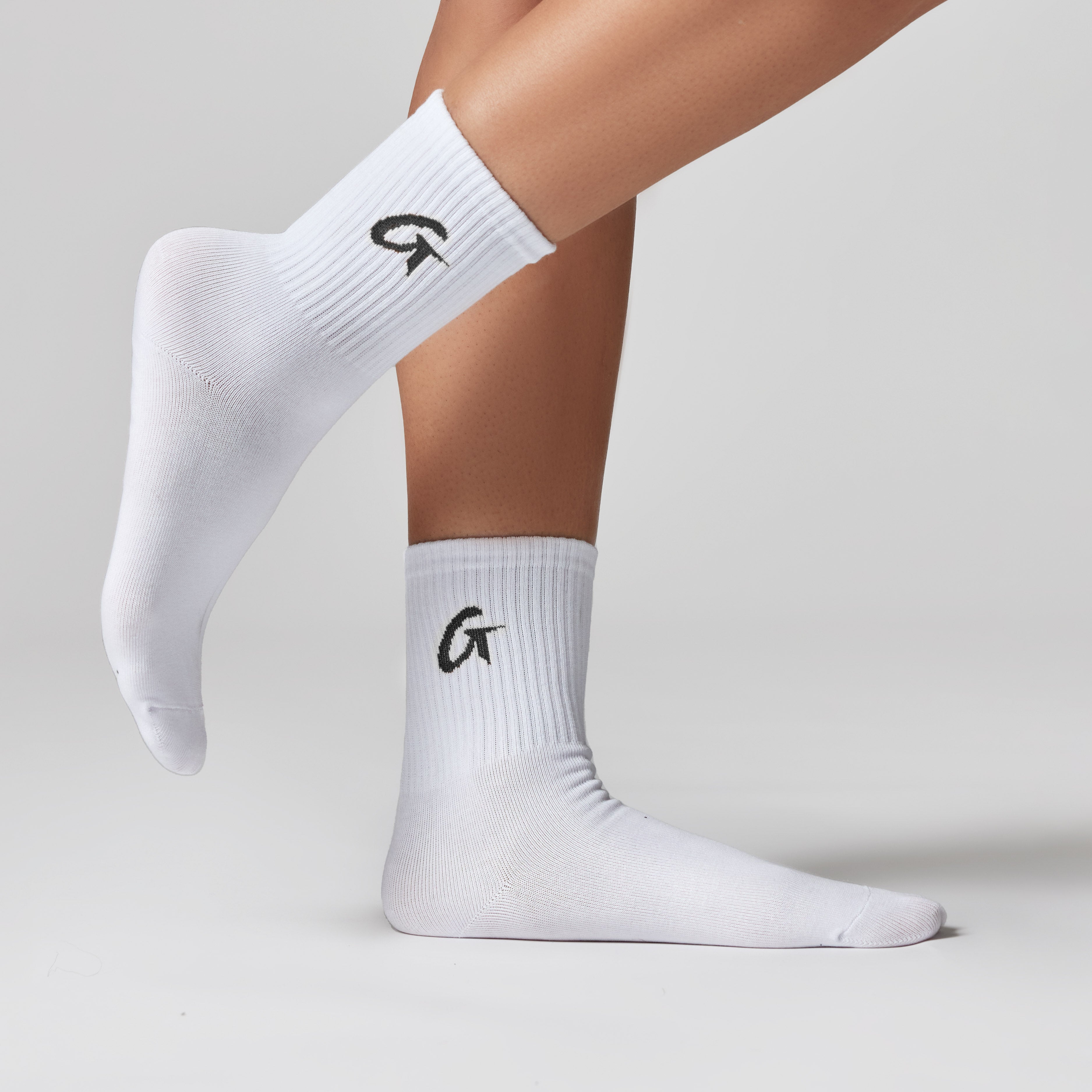 White crew socks with black "G" logo, ribbed texture, and mid-calf length for stylish, affordable luxury accessories.