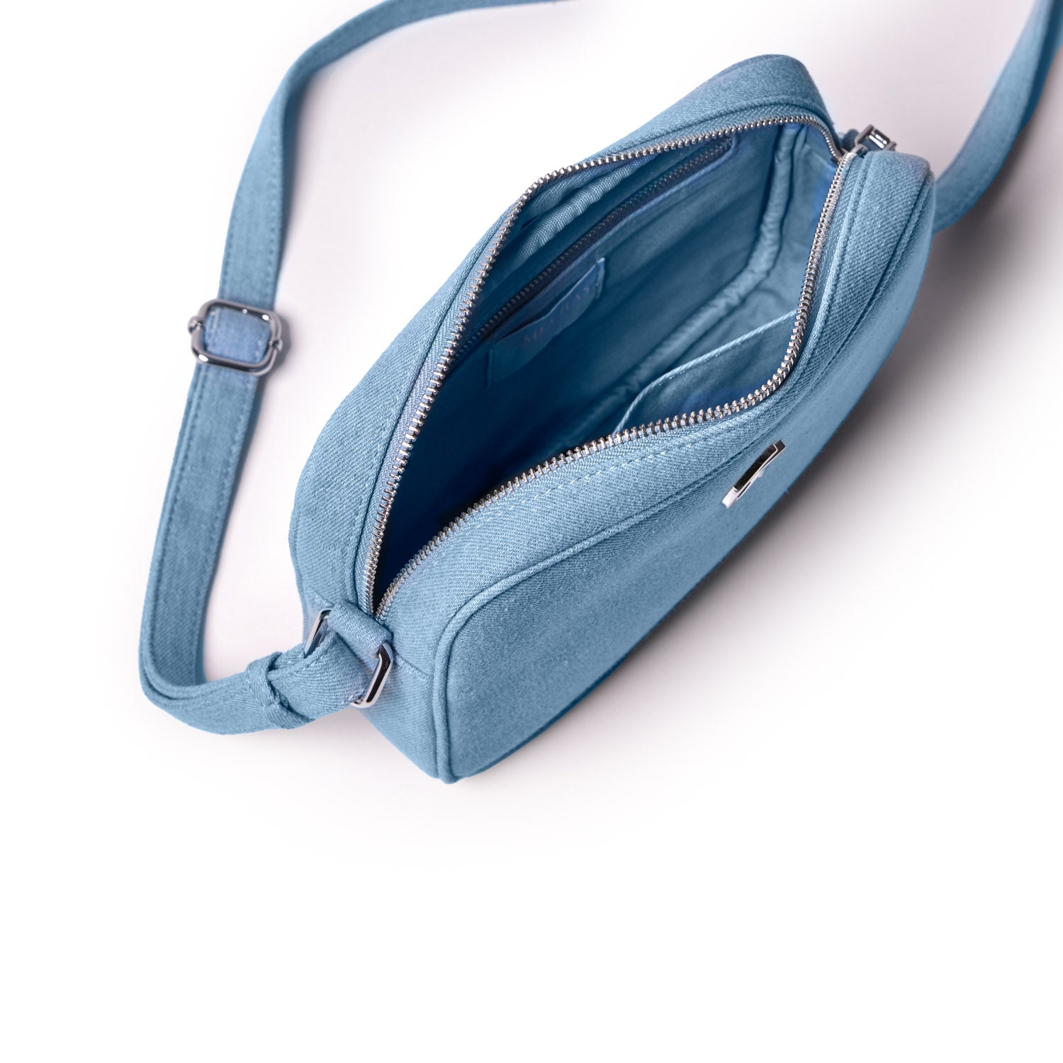 Blue denim camera bag with silver zipper, interior compartments, and adjustable strap, designed for carrying camera gear.