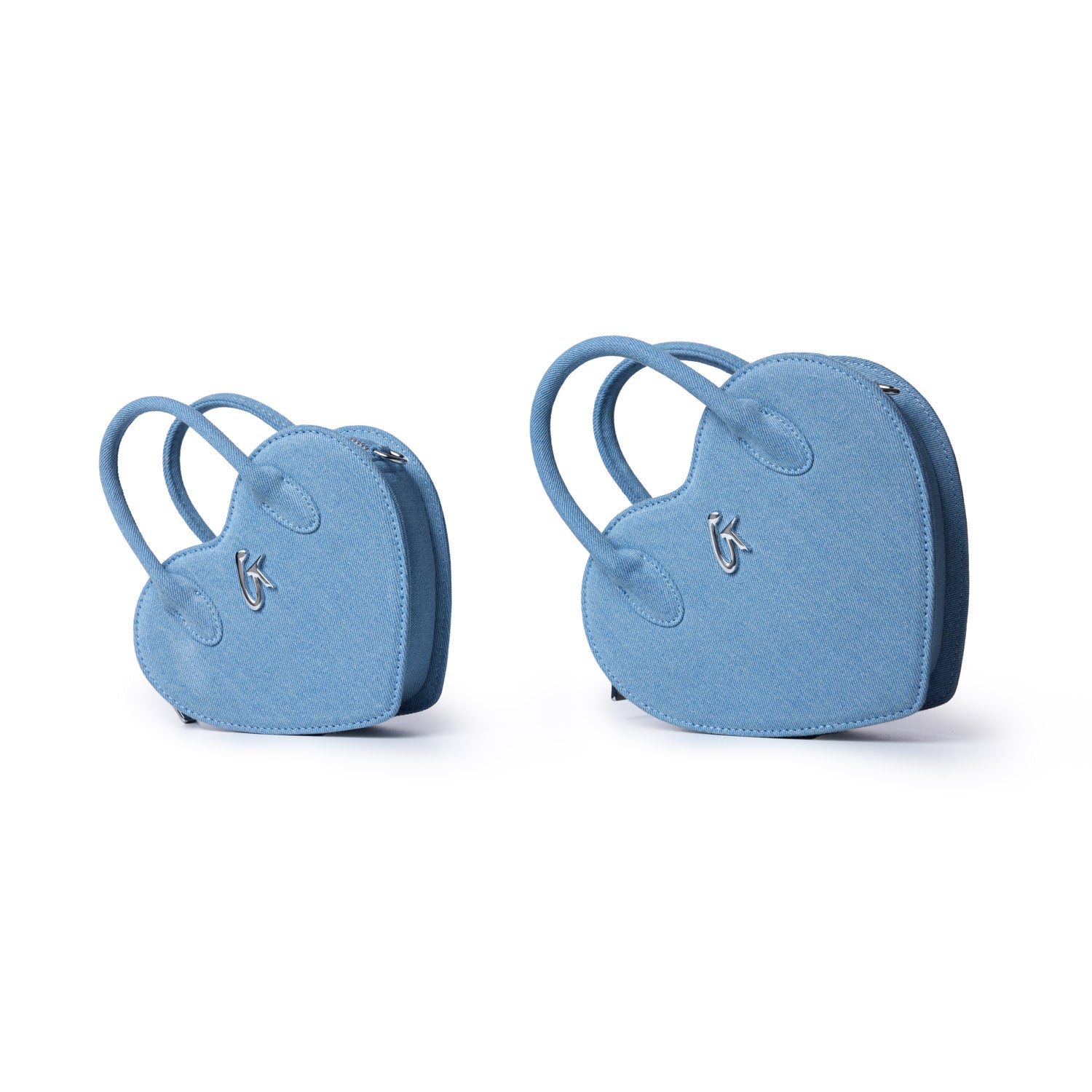 Pair of mini denim heart-shaped bags with handles, silver logo detail, and zip closure, in light blue color.