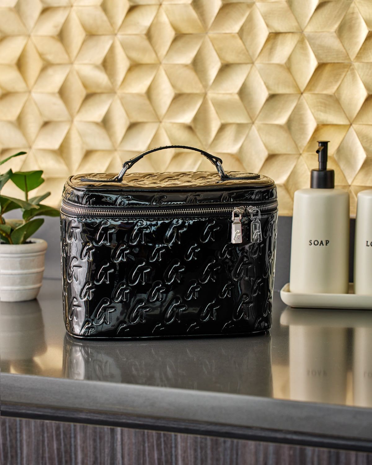Black glossy handbag with embossed G pattern, silver zipper, and top handle, set against a textured gold background.