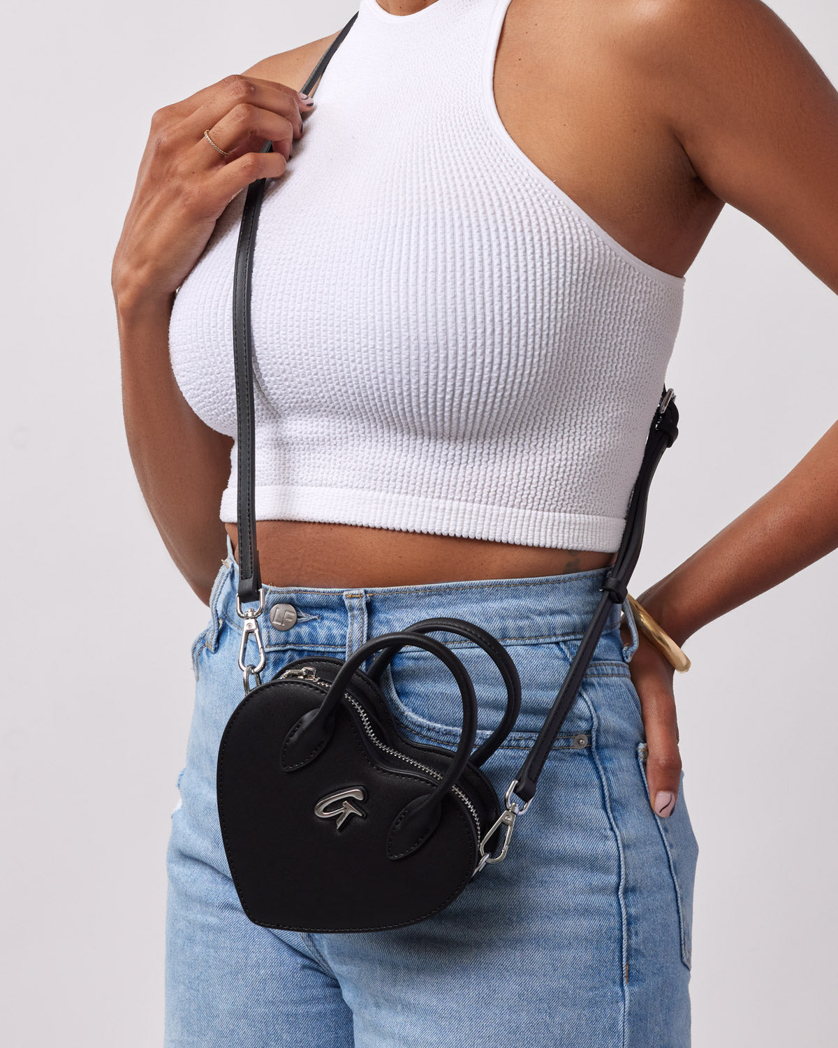 Mini heart-shaped black handbag worn crossbody, featuring a sleek design and adjustable strap, perfect for stylish outings.