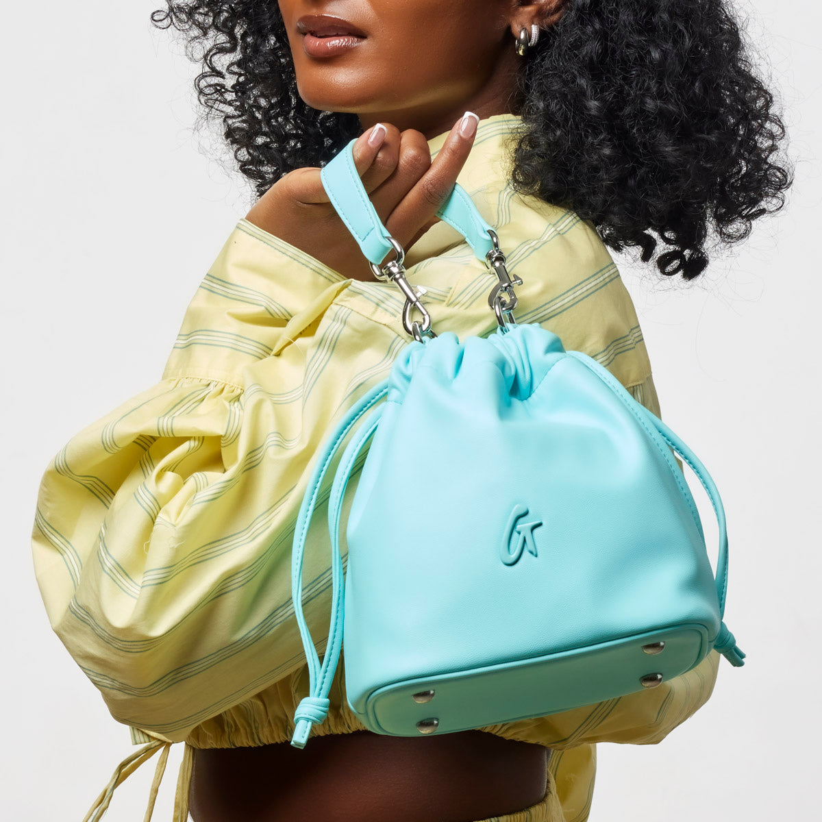 Teal mini drawstring bucket bag held by a model, featuring a stylish design and adjustable straps.