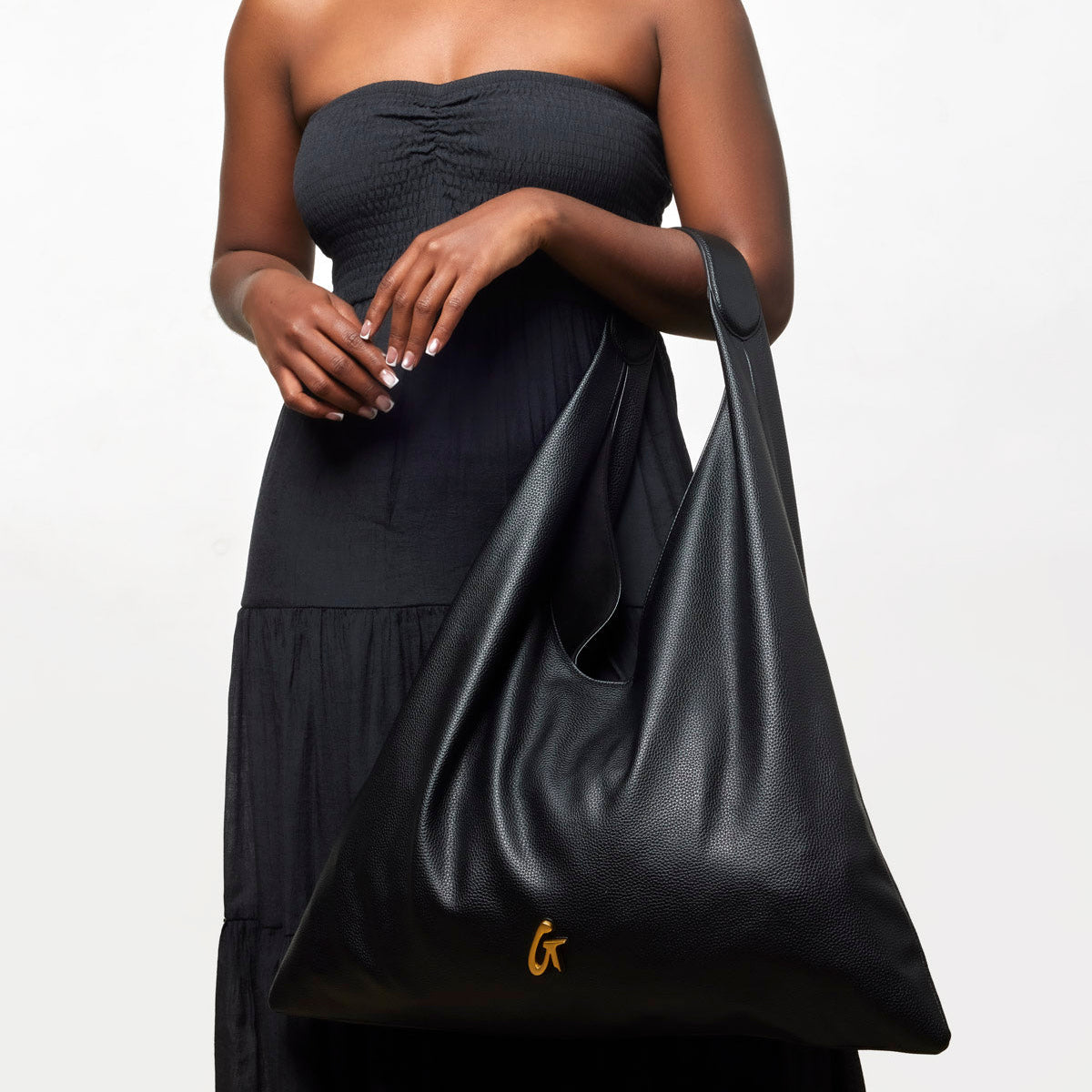 Black pebble hobo shoulder bag held by a woman in a strapless dress, featuring a stylish, slouchy design.