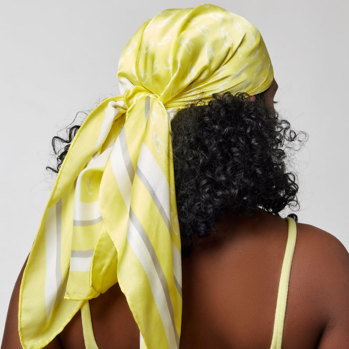 Large yellow monogram silk scarf tied at the back, showcasing a stylish and vibrant accessory for any outfit.