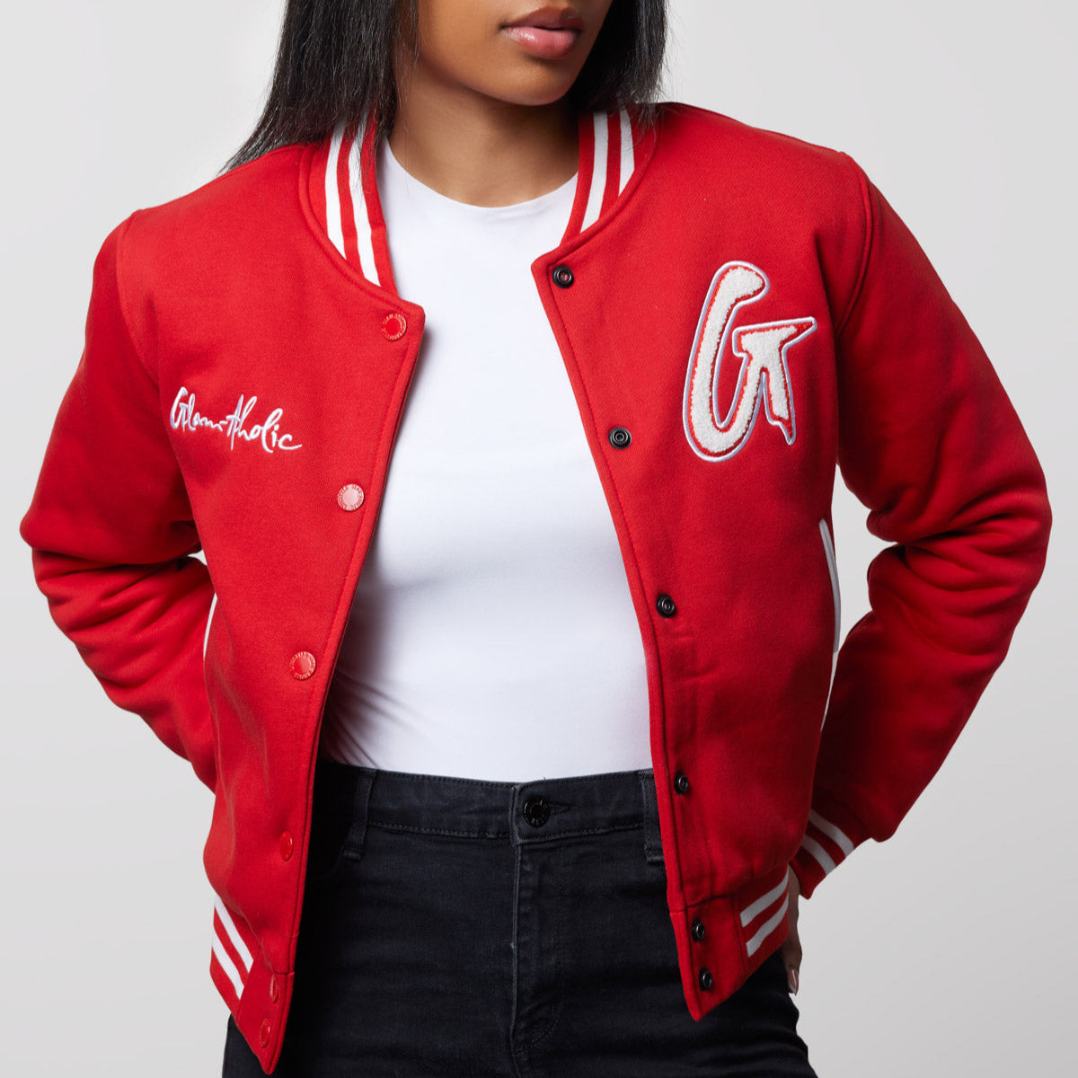 Red varsity jacket with white striped cuffs and collar, embroidered patches, and snap buttons, styled with a white t-shirt and black jeans.