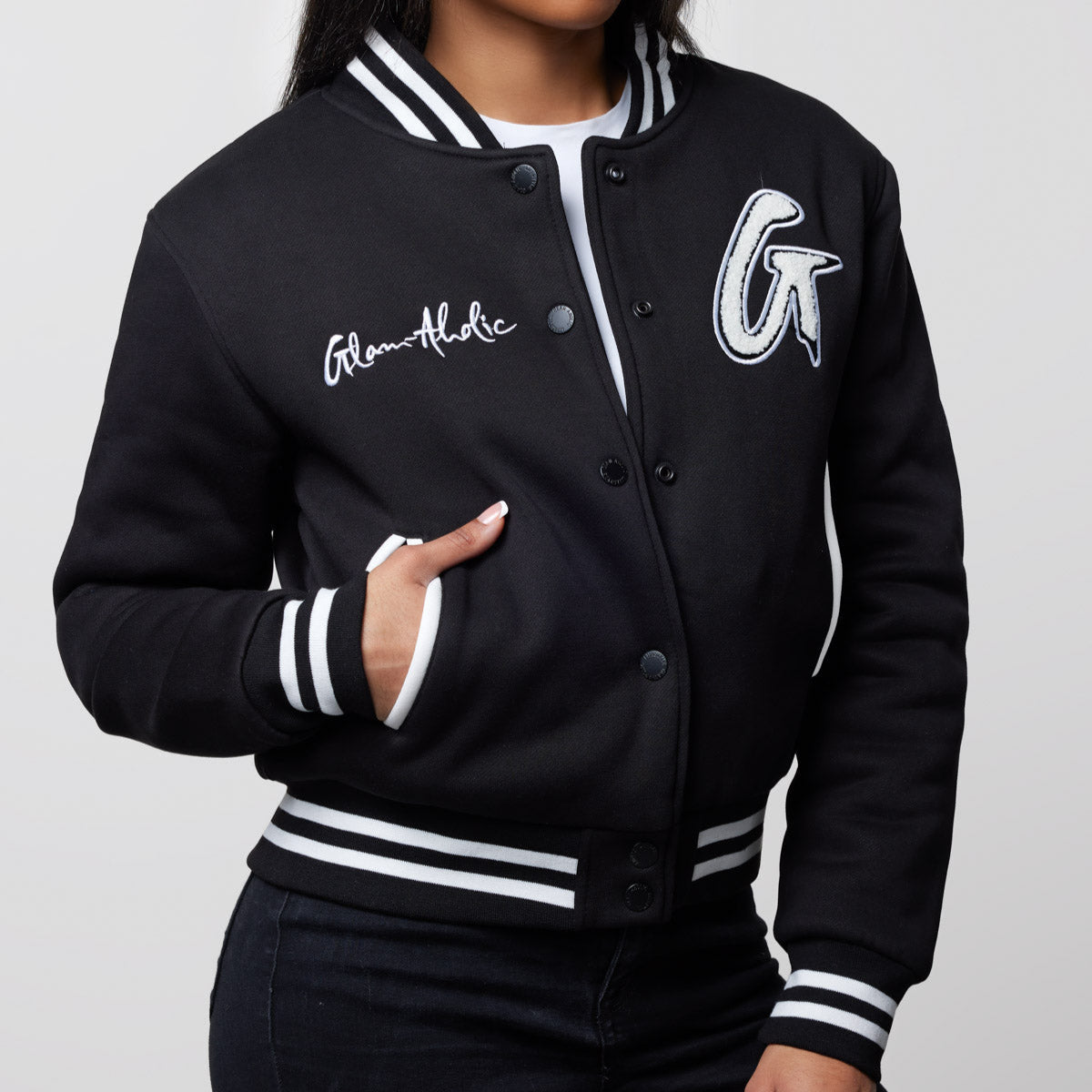 Black varsity jacket with white striped cuffs, collar, and hem, featuring "Glam-Aholic" embroidery and large letter patches.