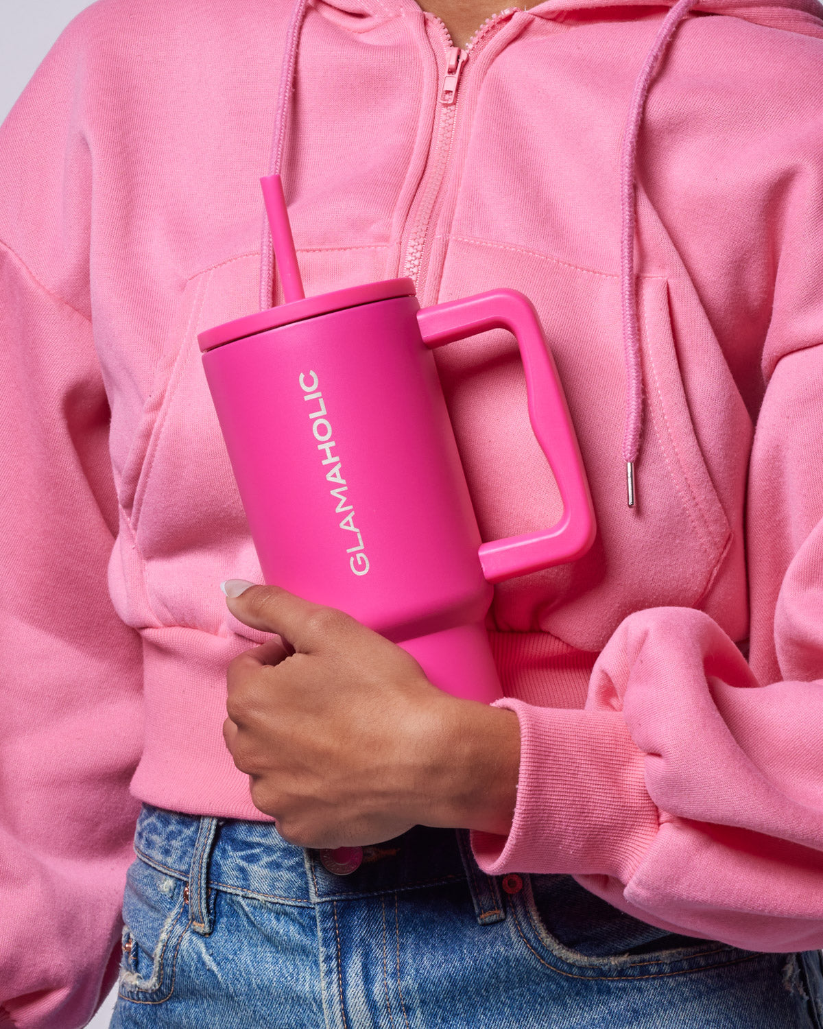 Hot pink athletic tumbler held by a person wearing a pink hoodie, showcasing its sleek design and straw.