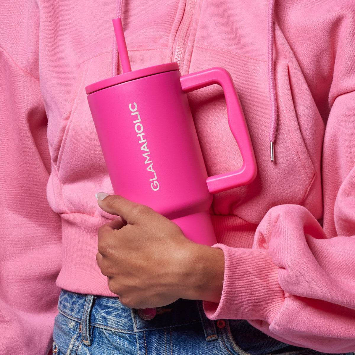 Hot pink athletic tumbler held by a person wearing a pink hoodie, showcasing its sleek design and straw.