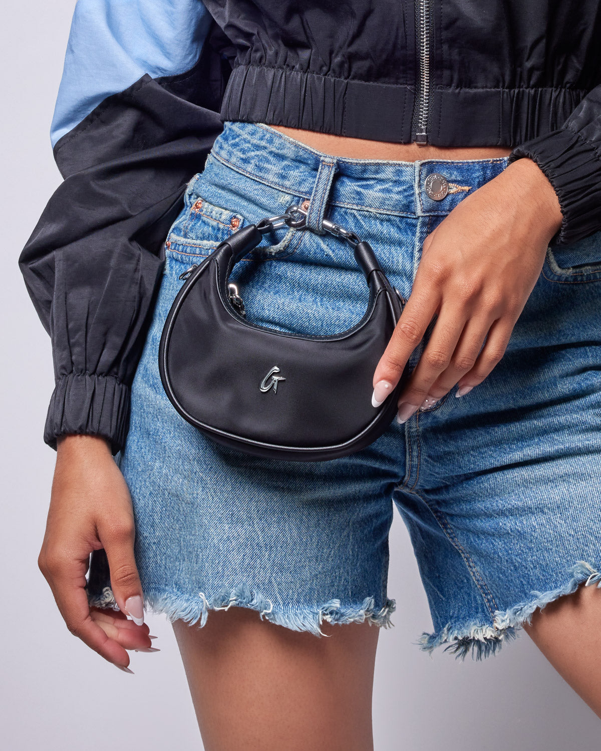 A person holds a black nano nylon hobo bag with a curved handle, paired with denim shorts and a sporty jacket.