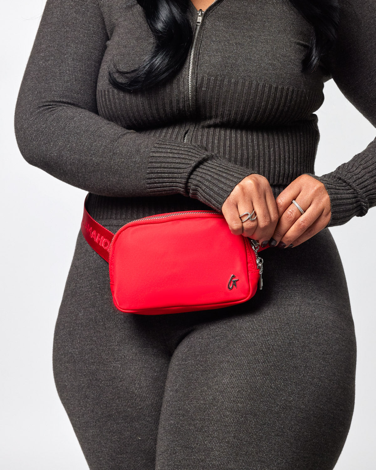Red nylon fanny pack worn around the waist of a person dressed in a dark gray zip-up sweater and matching leggings.