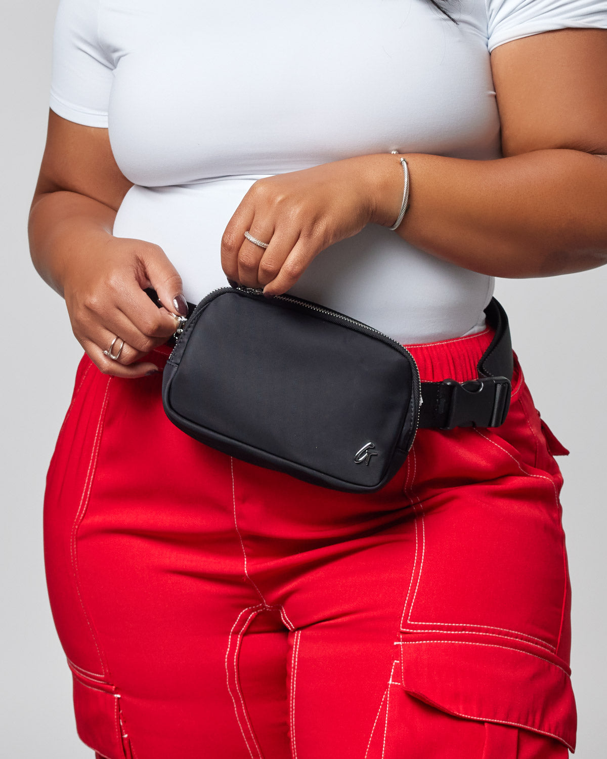 Black nylon fanny pack worn around the waist of a person dressed in a white top and red pants.