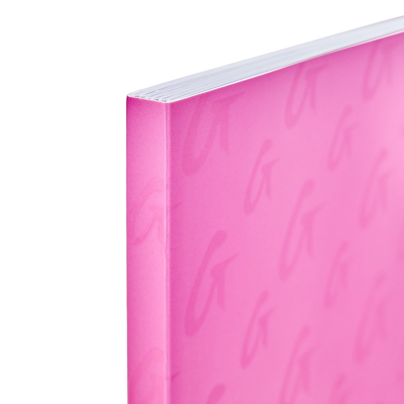 Close-up of a hot pink monogram notebook with a smooth cover and subtle cursive pattern, showing the top edge and corner.
