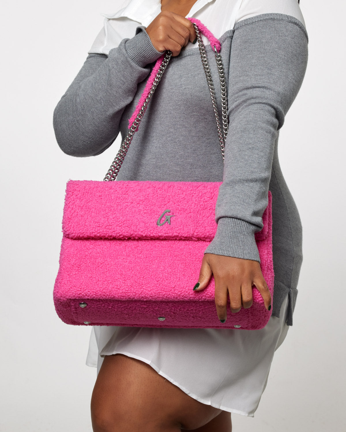 Large hot pink teddy flap bag with chain strap, featuring a silver logo on the front, held by a woman in casual clothing.