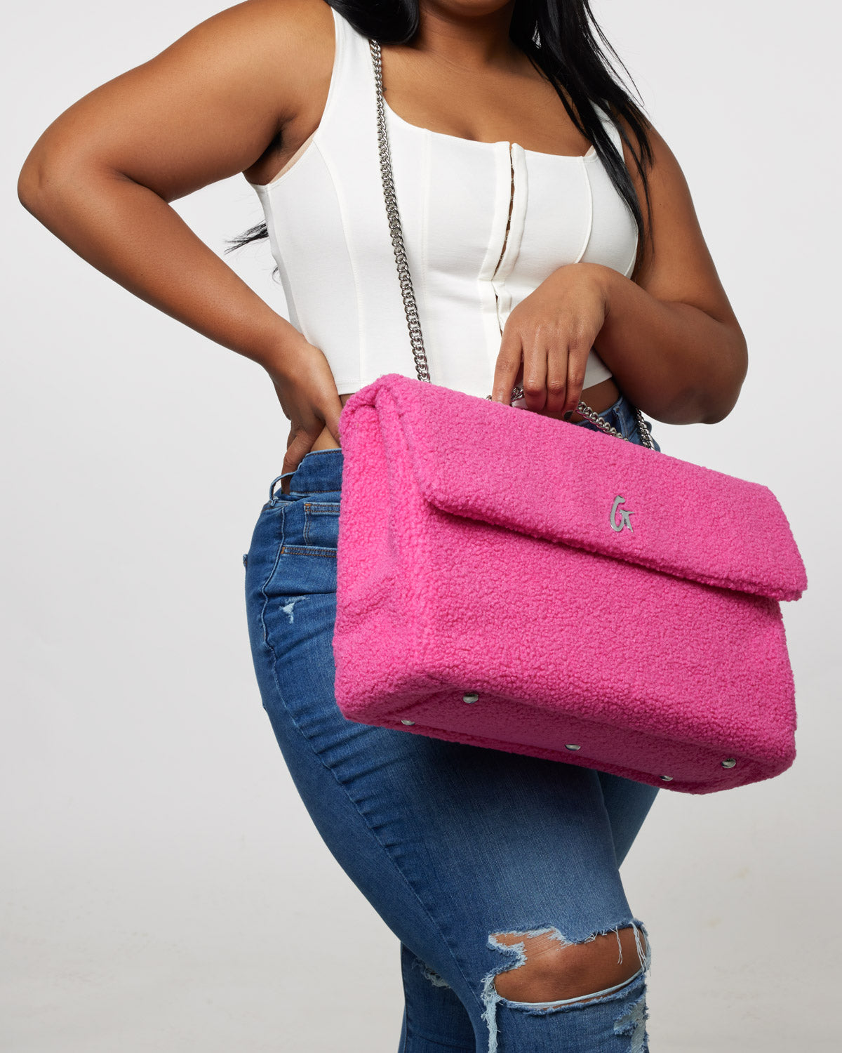 Large hot pink teddy flap bag with chain strap, worn by a woman in a white top and ripped jeans.