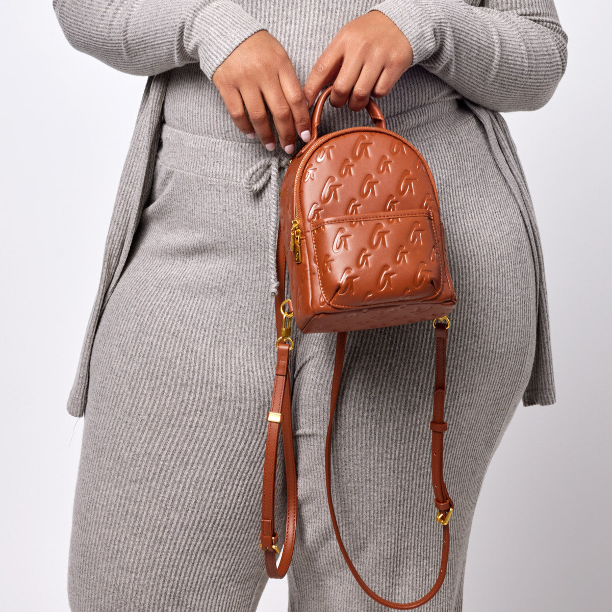 Small caramel-colored handbag with embossed G pattern, gold hardware, and adjustable strap, styled with neutral loungewear.