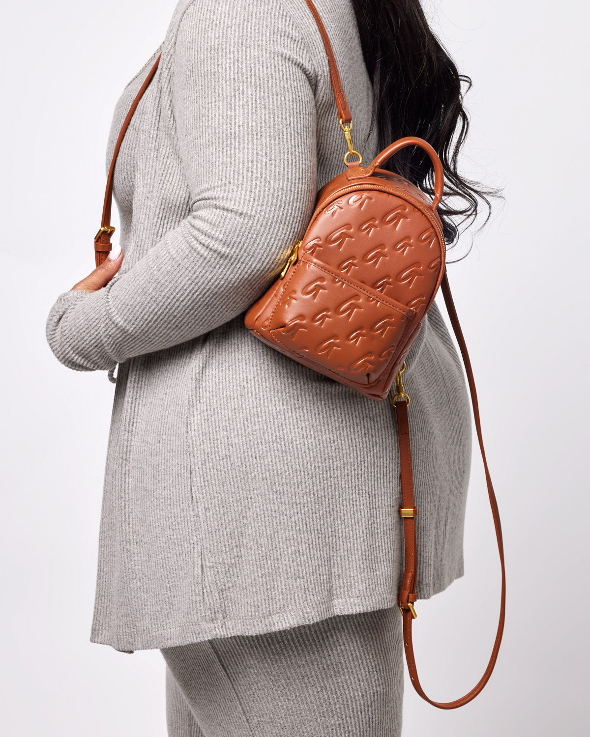 Brown mini monogram backpack with embossed G pattern, worn over a beige knit sweater and matching pants.