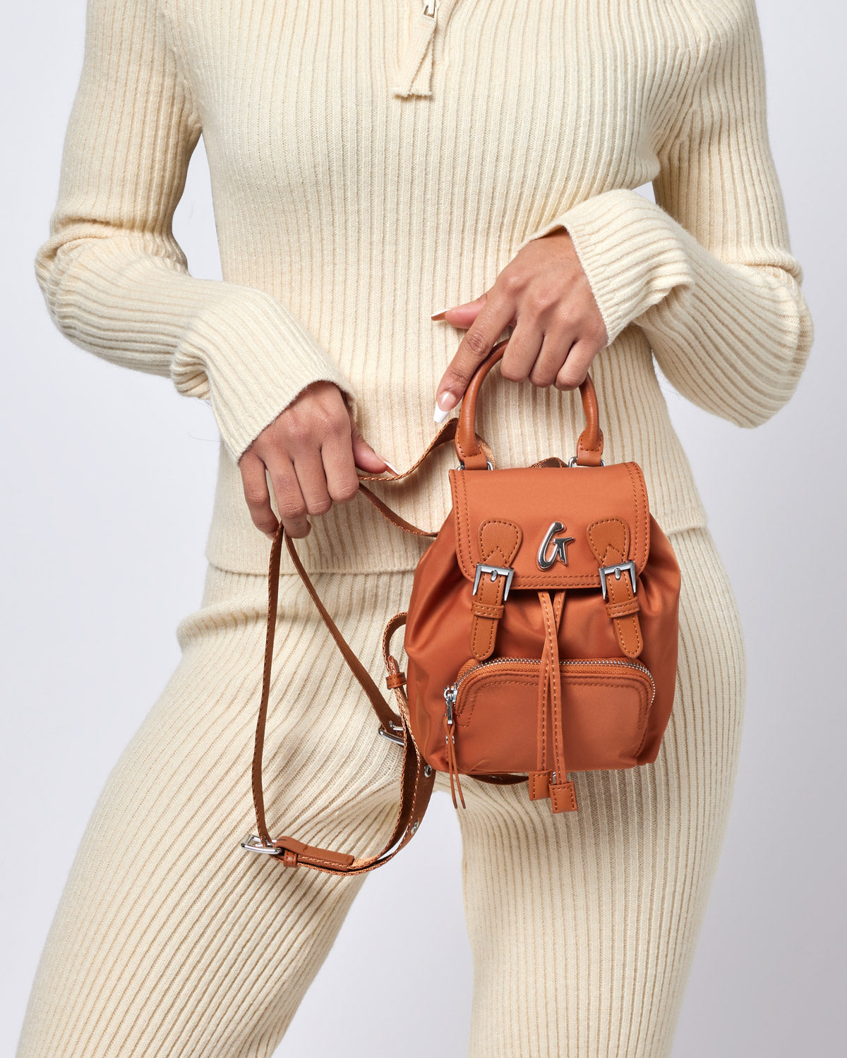 Mini nylon backpack in brown with top handle, front zipper pocket, adjustable strap, and silver hardware details.