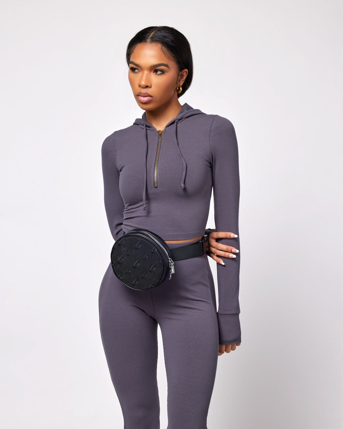 Black mesh monogram fanny pack worn around the waist of a woman dressed in a matching gray athletic outfit.