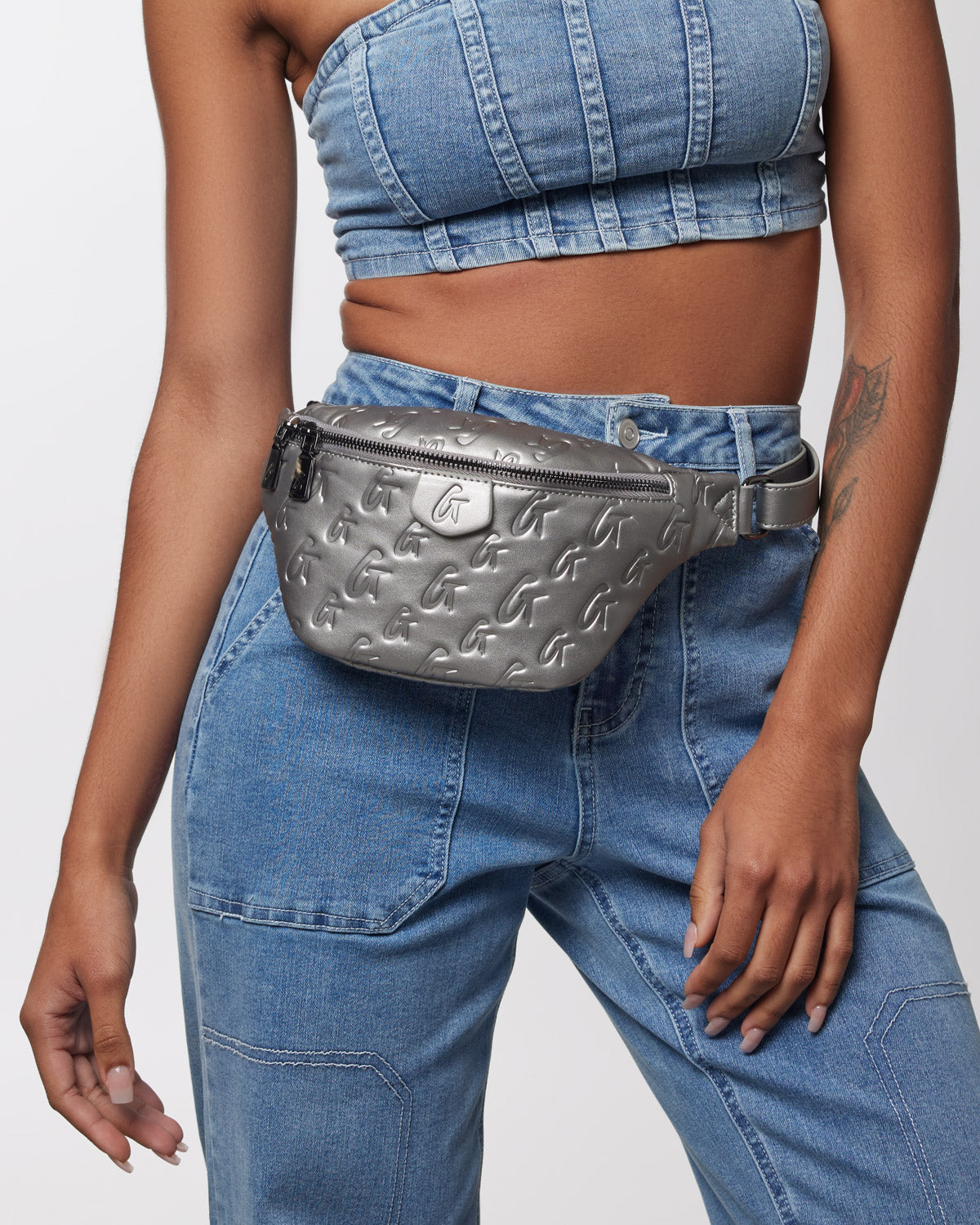 Silver embossed waist bag with black zipper, worn around the waist over a denim crop top and jeans, for affordable designe...