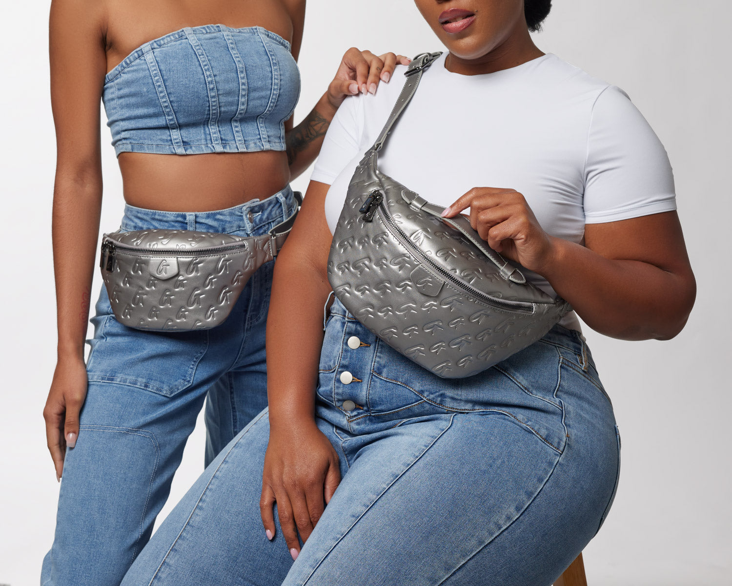 Stylish women wearing denim outfits showcase the MINI MONOGRAM FANNY PACK in platinum, highlighting its chic design.
