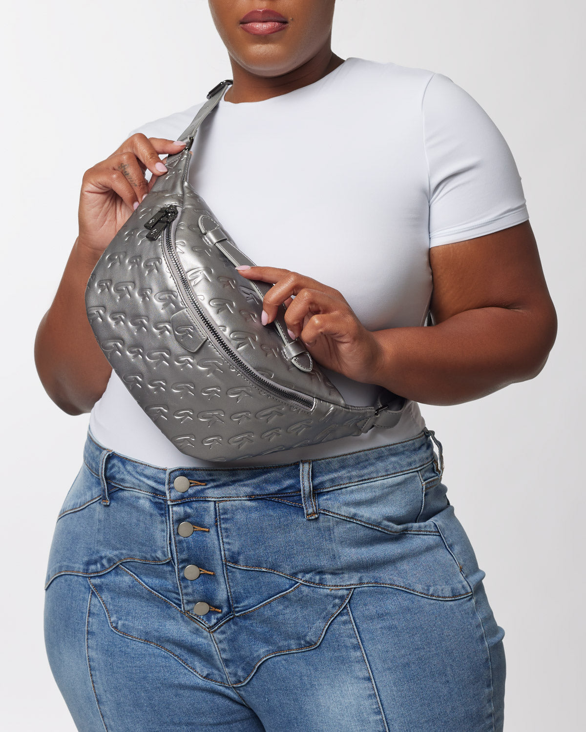 Gray designer-style sling bag with embossed logo pattern, silver zippers, and adjustable strap, worn crossbody.