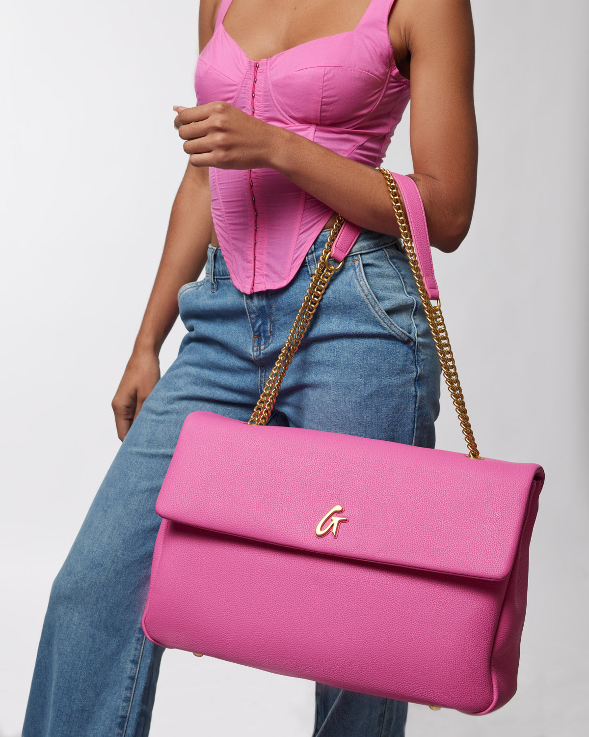 Large hot pink pebble-textured flap bag with a gold chain strap and a gold "G" logo on the front.
