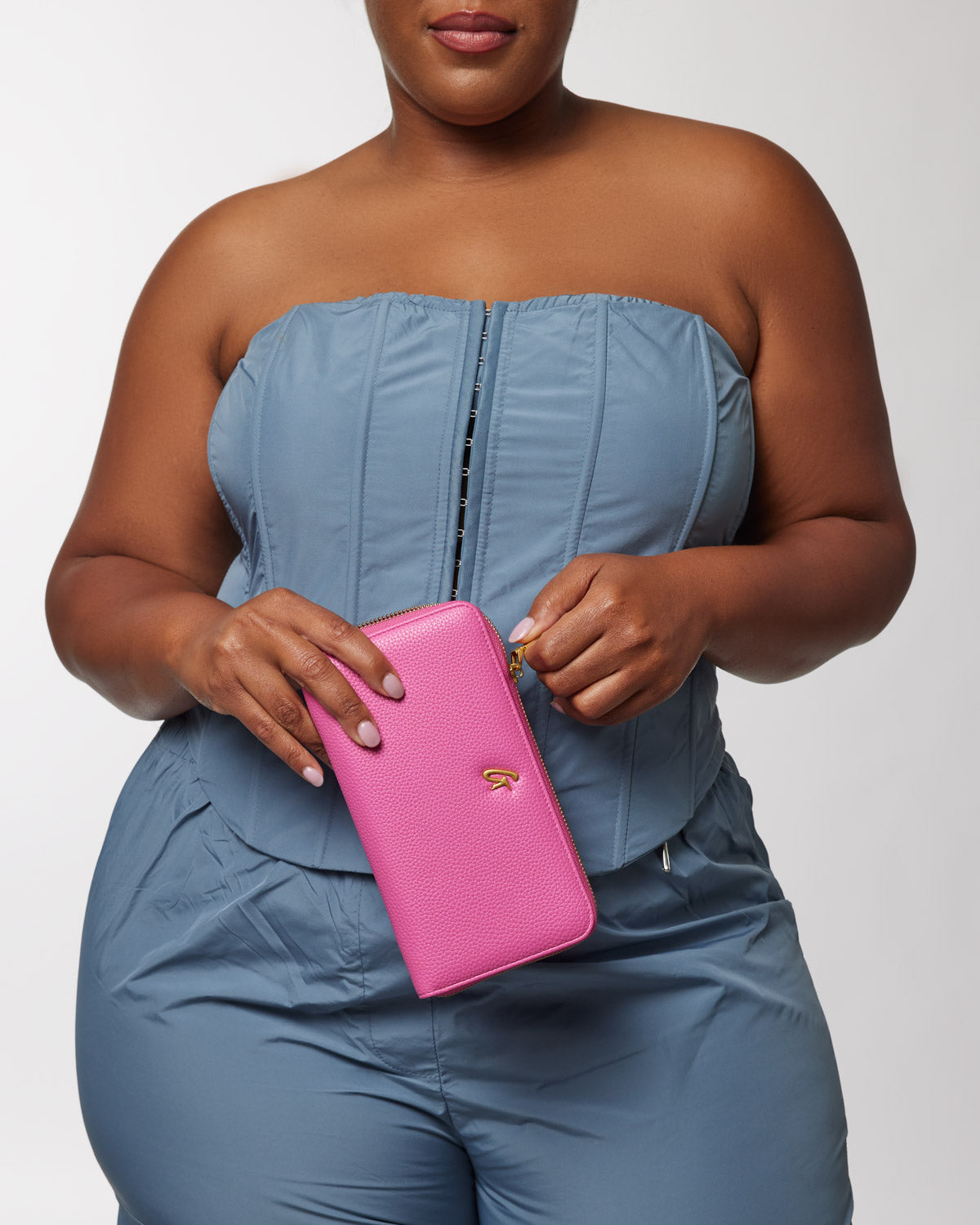 Jumbo pebble wallet in hot pink with a textured surface, gold logo, and zipper closure, held by a woman in a blue strapless top.