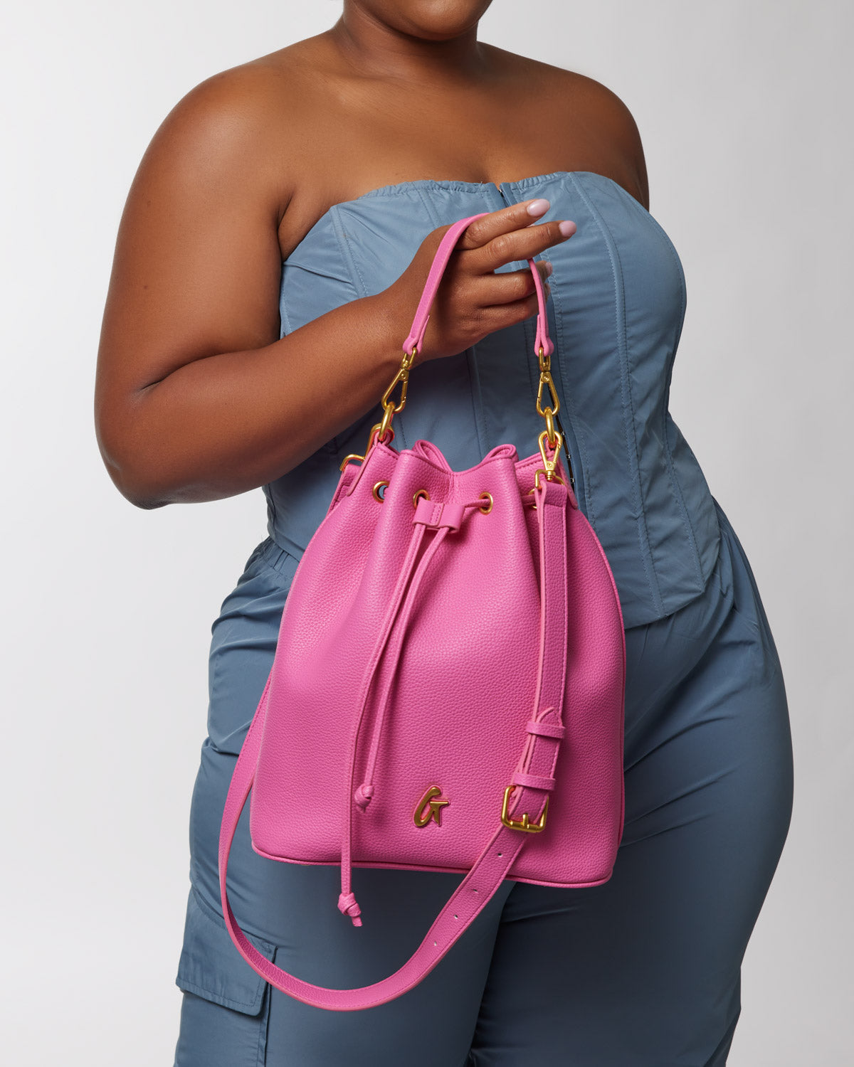 Pink textured leather bucket bag with gold hardware, adjustable strap, and drawstring closure. Perfect for affordable luxu...