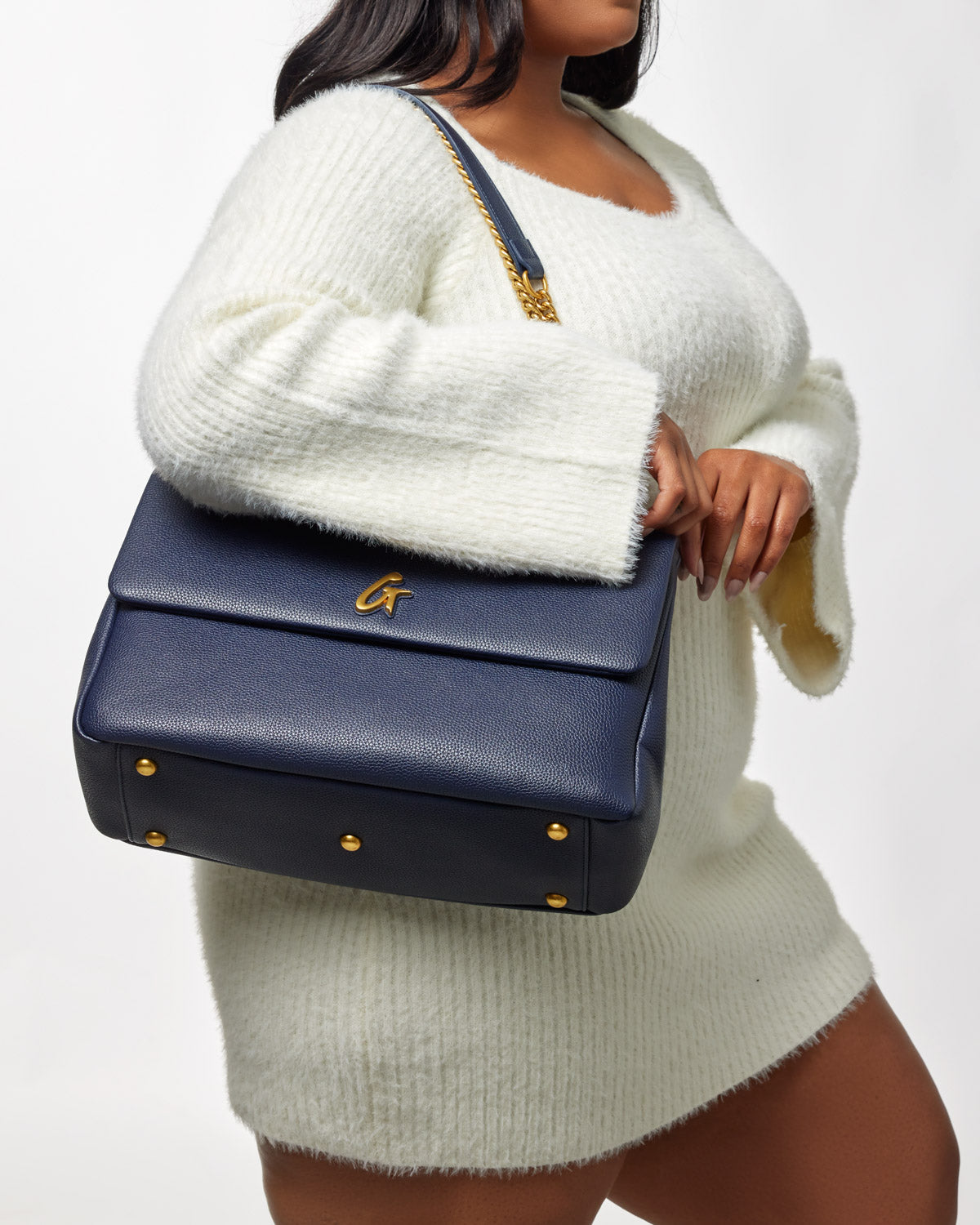 Large navy pebble flap bag with gold hardware, worn over a white sweater, featuring a structured design and textured leather.