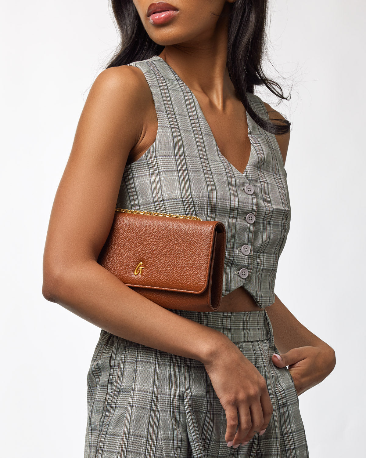 Brown Pebble Travel Wallet on a woman’s arm, featuring a gold chain and logo, with a plaid outfit.
