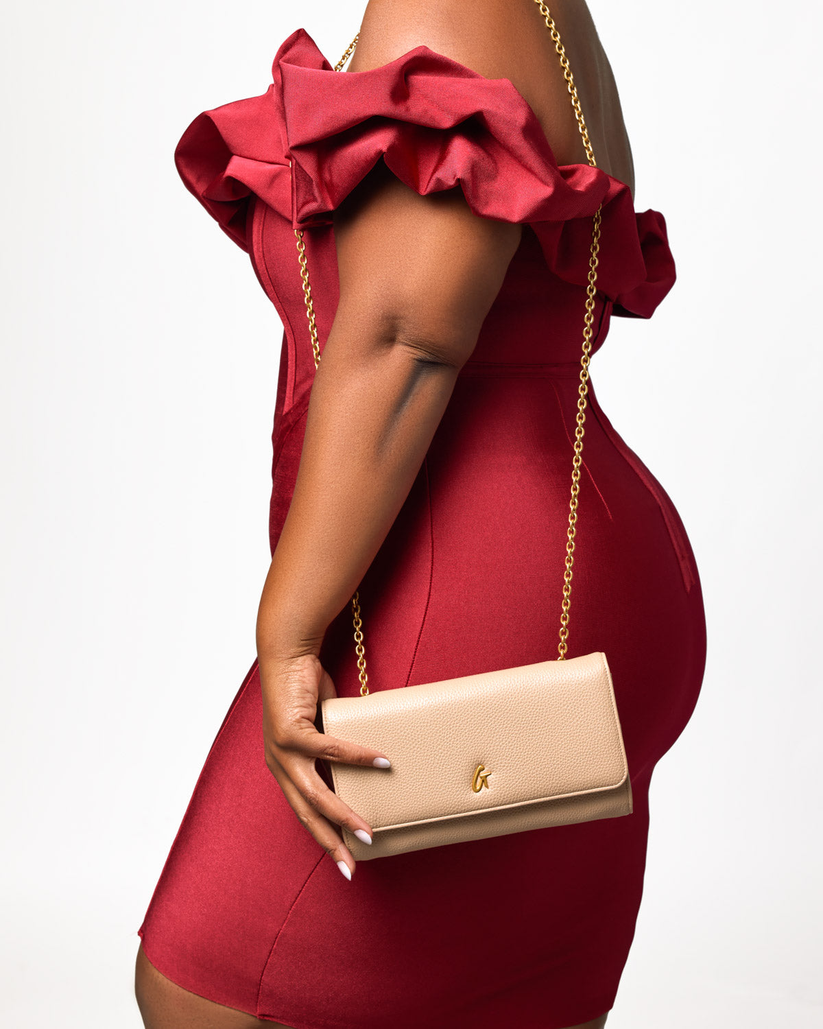 Beige Pebble Travel Wallet with gold chain, held by a woman in a red dress with ruffled shoulder details.