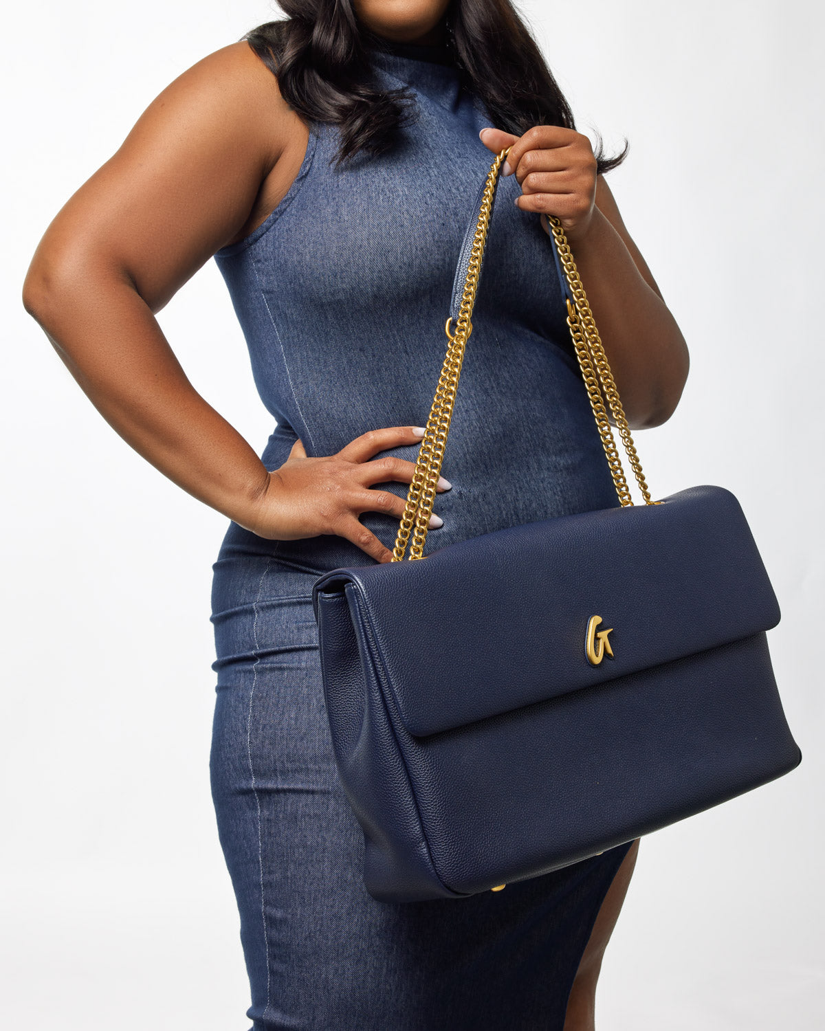A woman holds a navy XL Pebble Flap Bag with a gold chain strap, featuring a gold "G" logo on the front flap.
