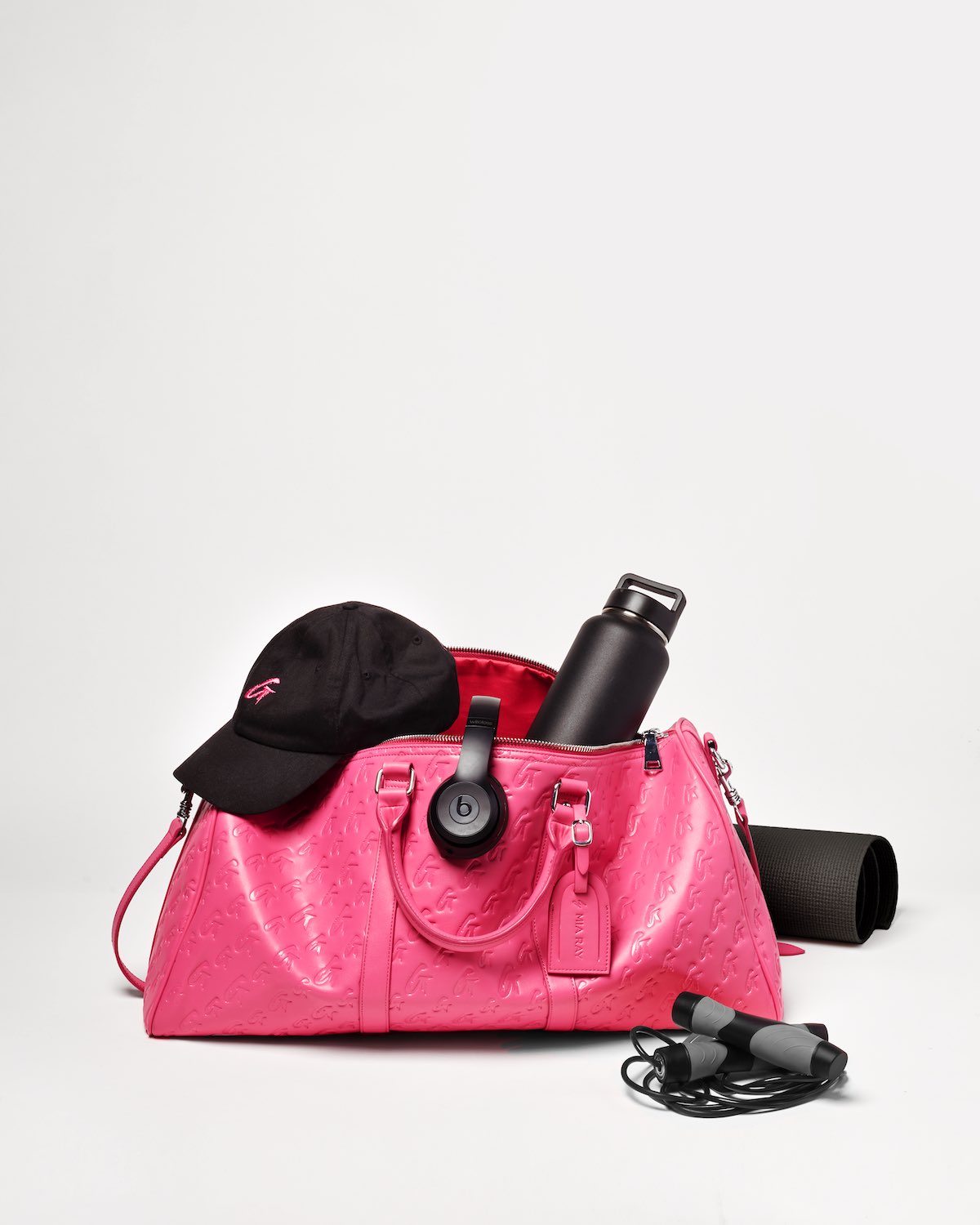Pink Monogram Duffle Bag with black headphones, water bottle, cap, and workout accessories on a white background.