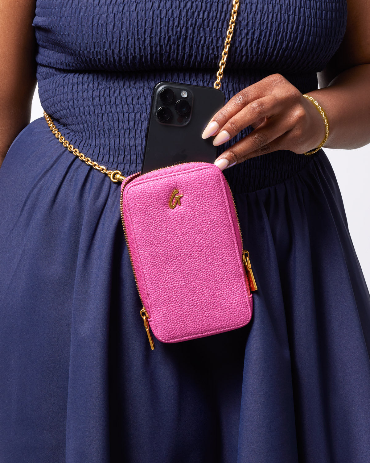 Pink Pebble Phone Crossbody bag with gold hardware, worn around the waist, holding a smartphone.
