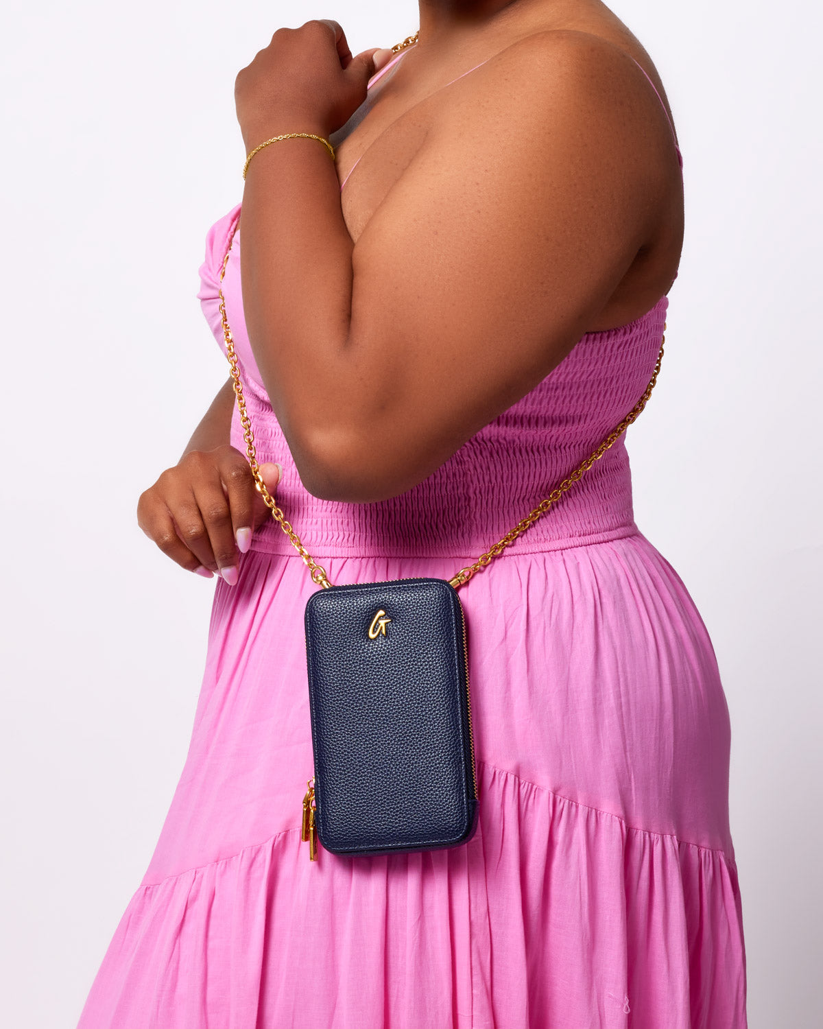 Navy Pebble Phone Crossbody bag with gold chain strap worn by a woman in a pink dress.