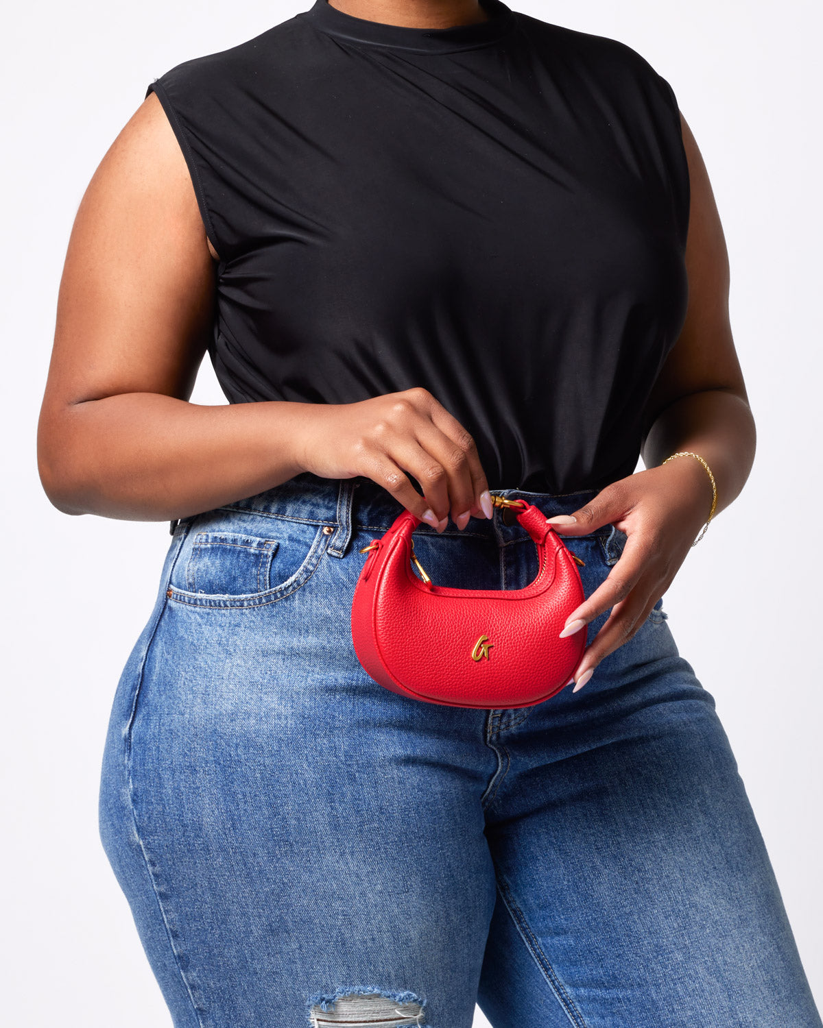 Red Nano Pebble Hobo Bag with gold hardware, held by a woman wearing a black top and blue jeans.
