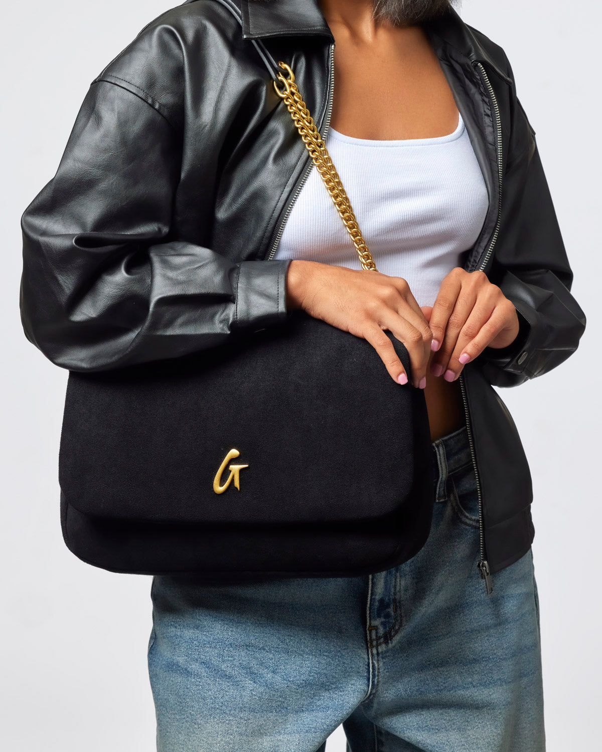 Medium black suede flap bag with gold chain strap, styled with a casual outfit featuring a leather jacket and jeans.