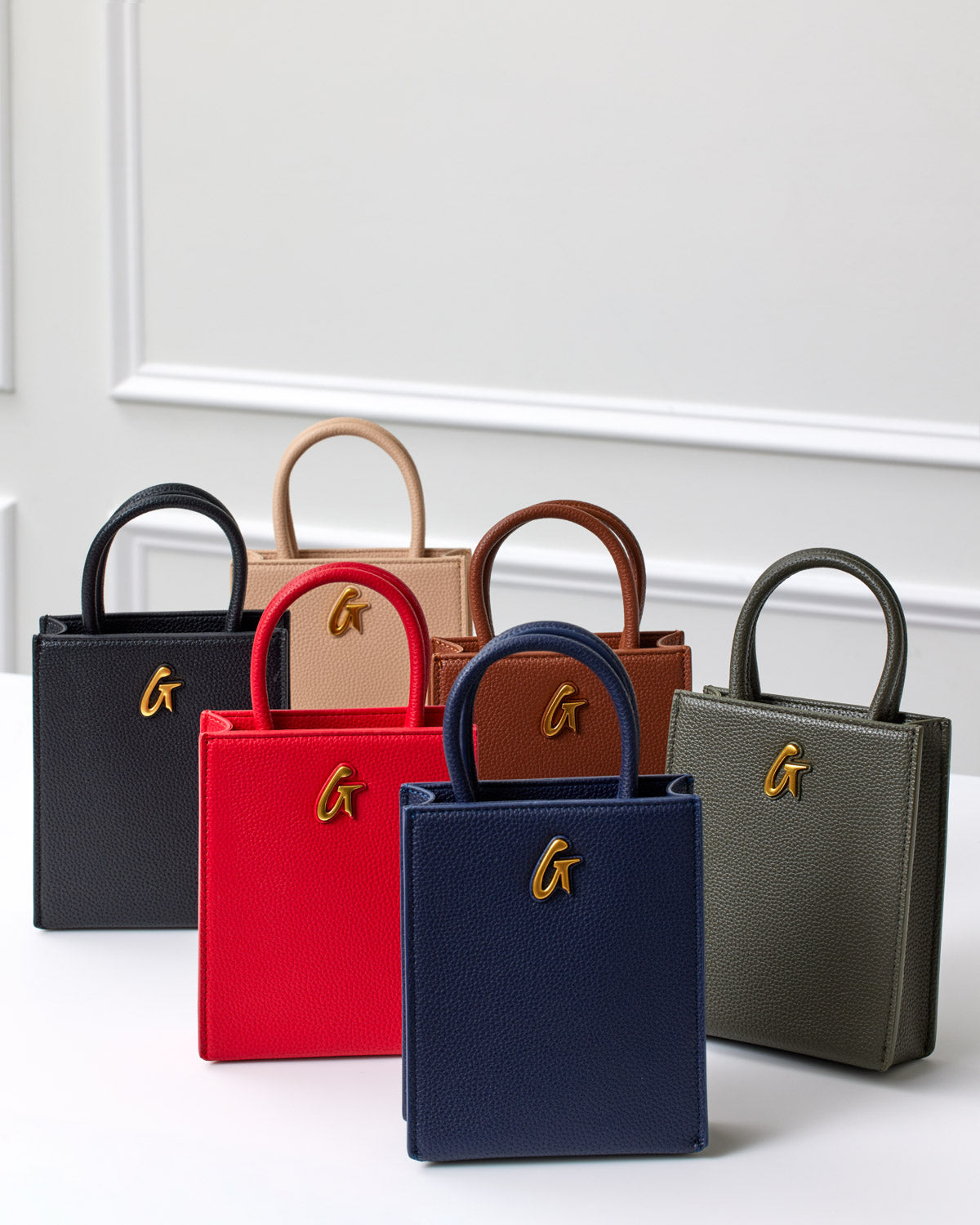 Set of six small textured handbags in black, red, navy, beige, brown, and green with gold "G" logo accents.