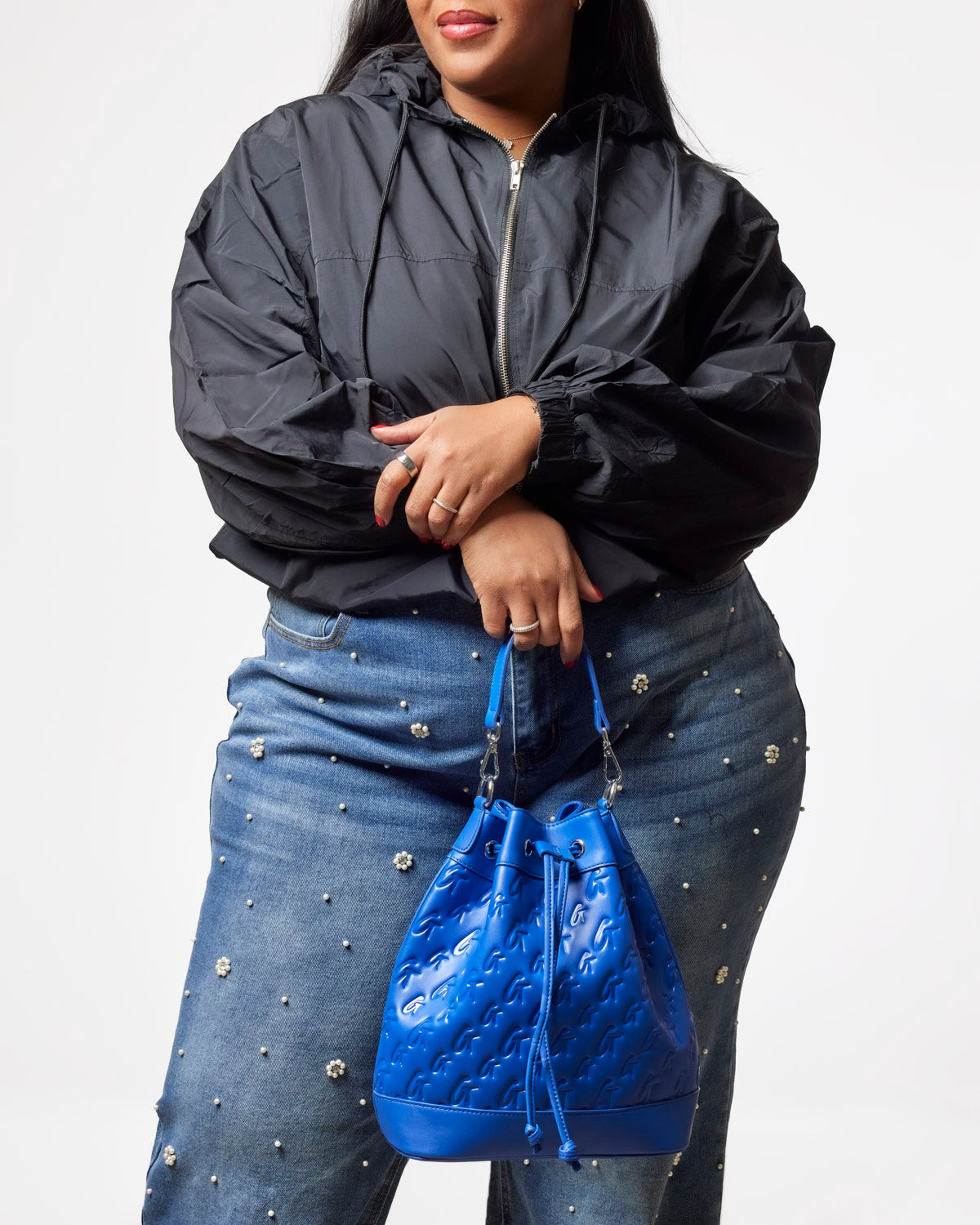 Large blue monogram bucket bag held by a woman in a black jacket and embellished jeans, showcasing stylish versatility.