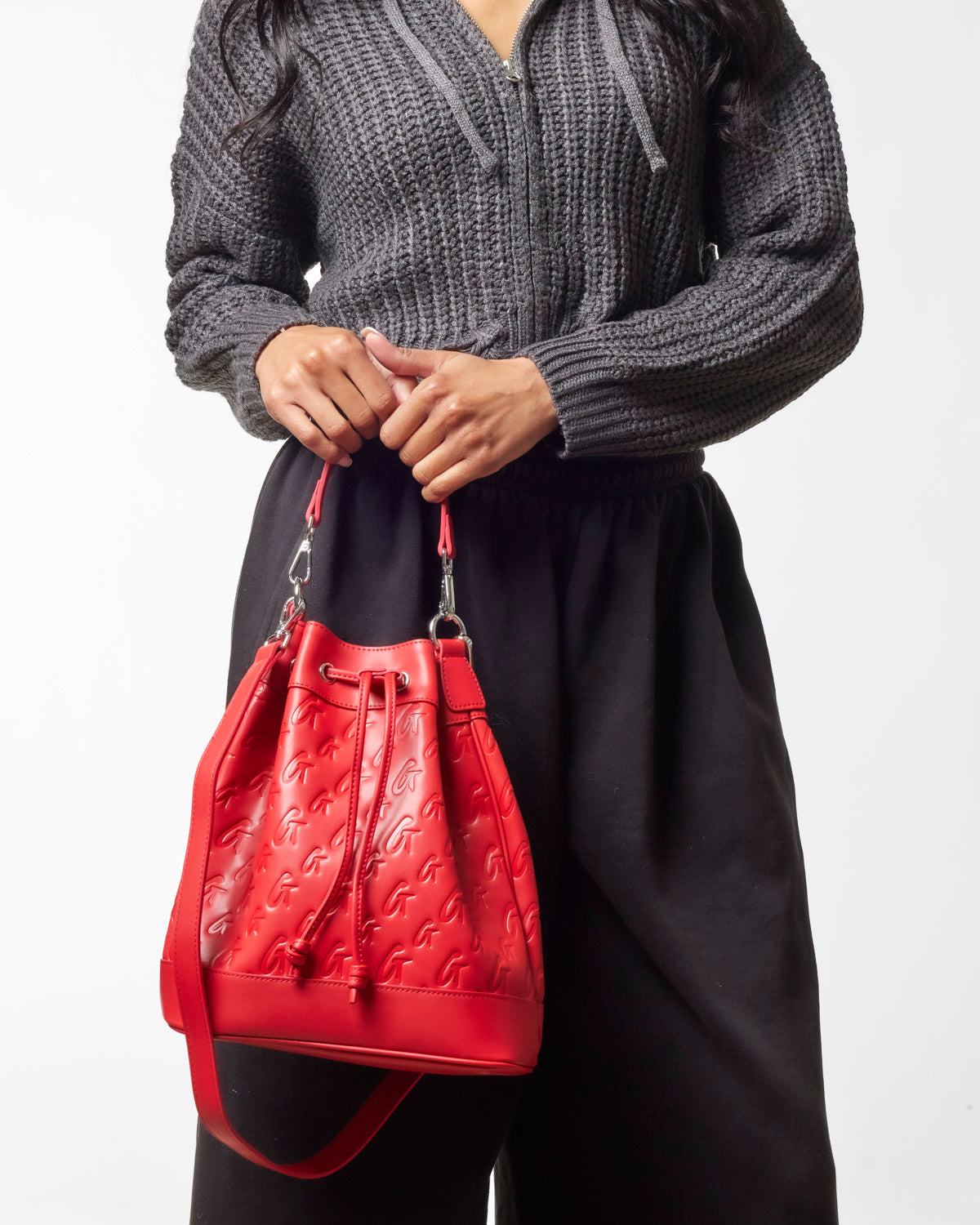 Red large monogram bucket bag held by a woman in a cozy sweater and relaxed pants, showcasing stylish design and versatility.