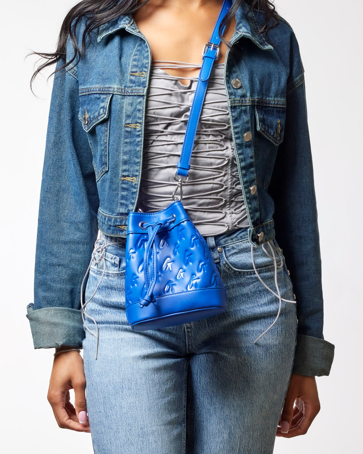 Mini monogram bucket bag in blue, featuring a drawstring closure, worn with a fitted top and denim jacket.