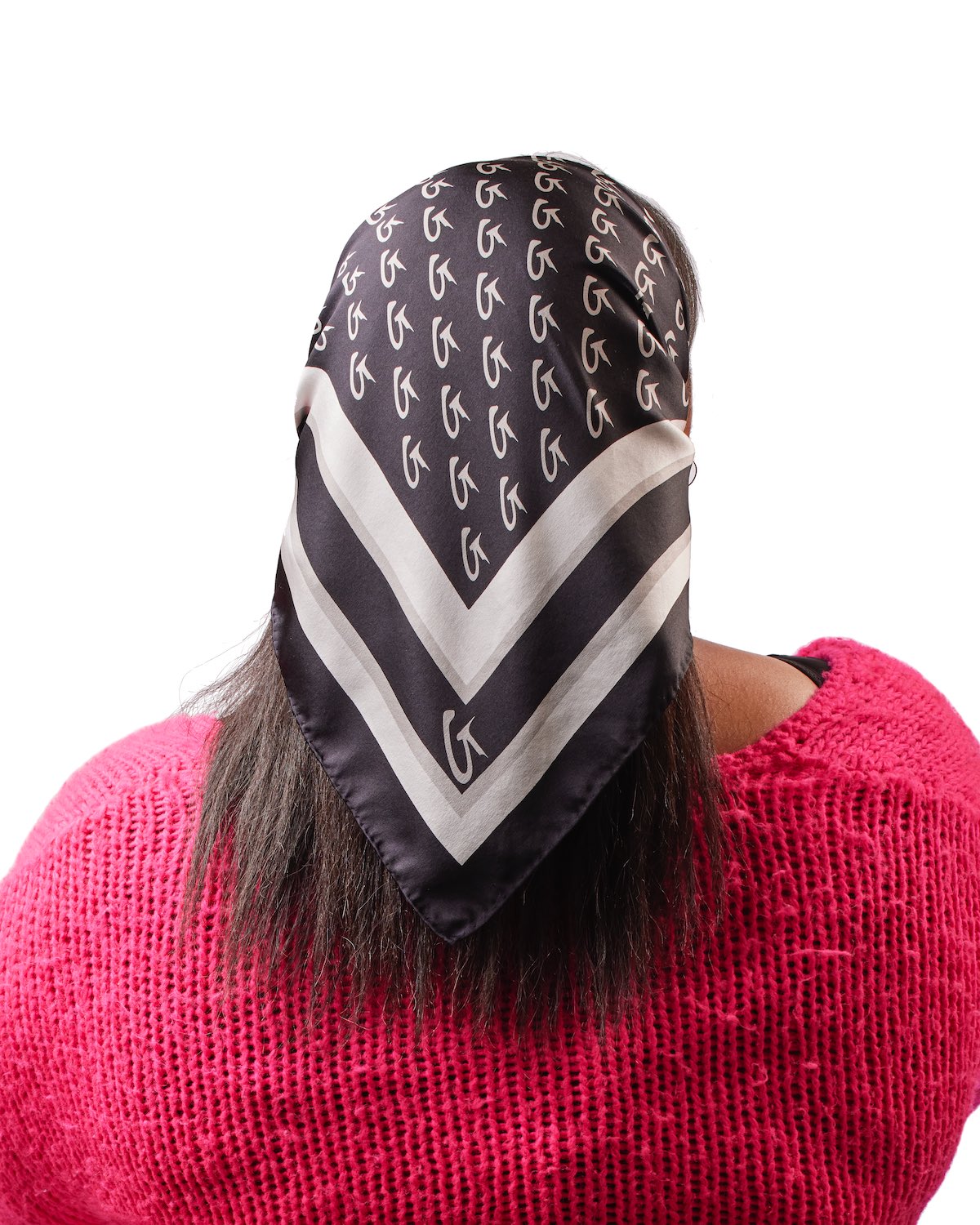 Large black silk scarf with monogram pattern, worn over a pink knitted sweater, featuring a white border and logo.