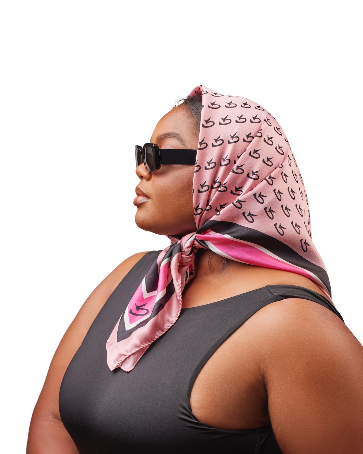 Close-up of a woman wearing a pink silk scarf with a monogram pattern, tied at the side, paired with black sunglasses and a black sleeveless top.
