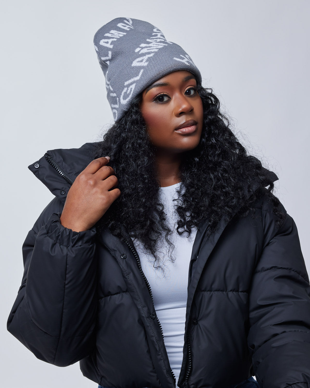 Woman wearing a gray Monogram Beanie, black puffer jacket, and white top, posing against a plain background.
