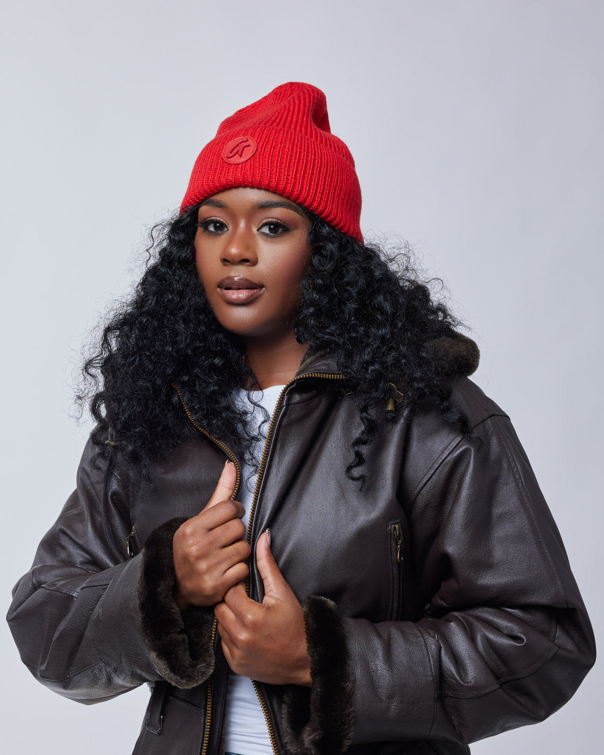 Woman wearing a red classic beanie hat, black curly hair, and a dark brown leather jacket with fur trim.