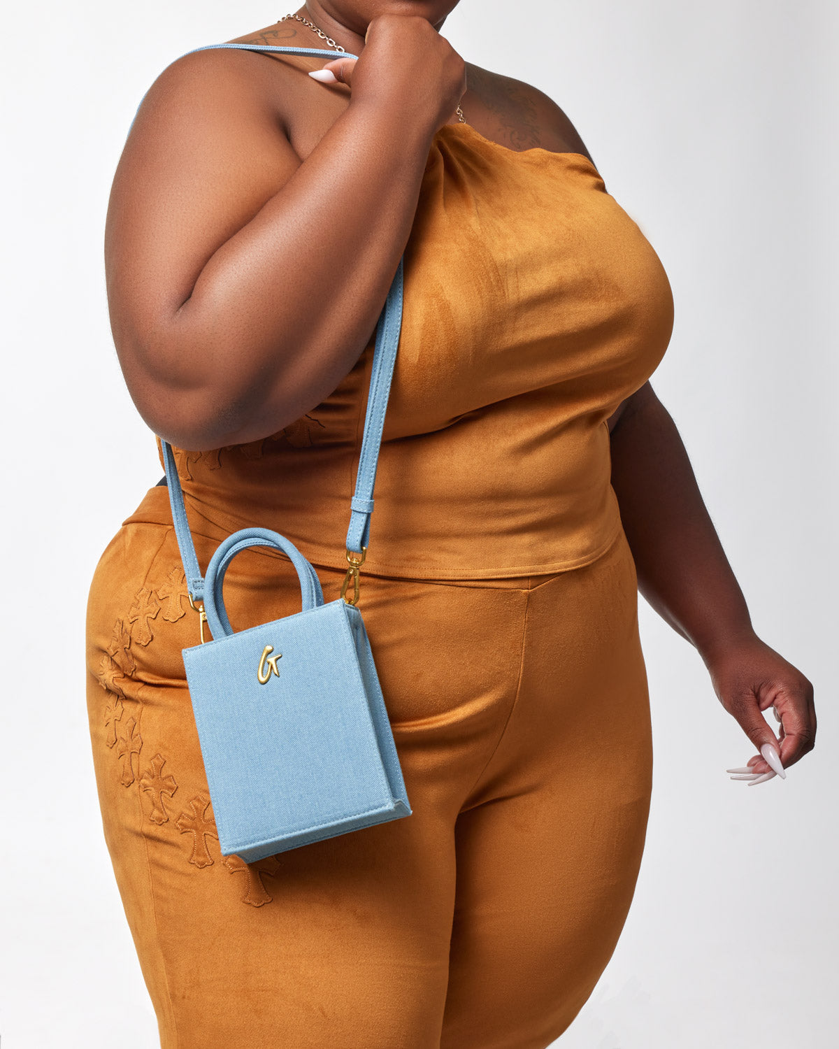 Mini denim gold tote bag with a small square shape, gold logo, and light blue strap, worn by a woman in matching outfit.