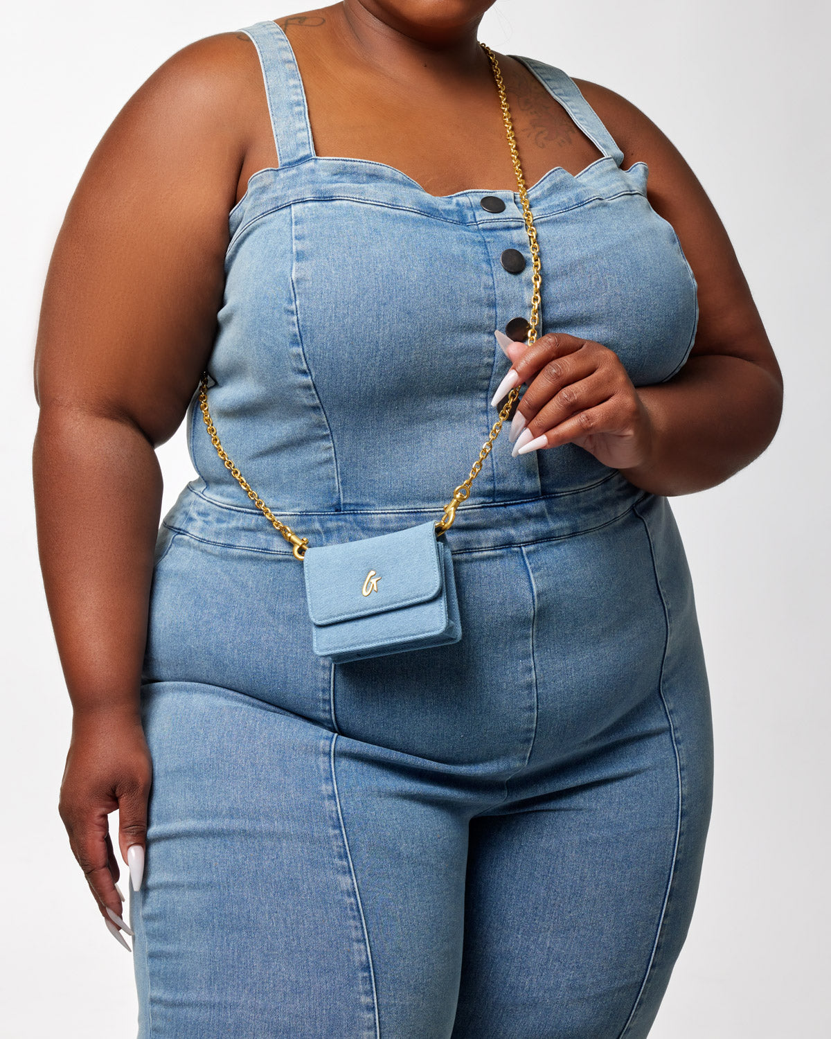 Close-up of a woman wearing a denim jumpsuit with a mini denim gold WOC purse on a gold chain.
