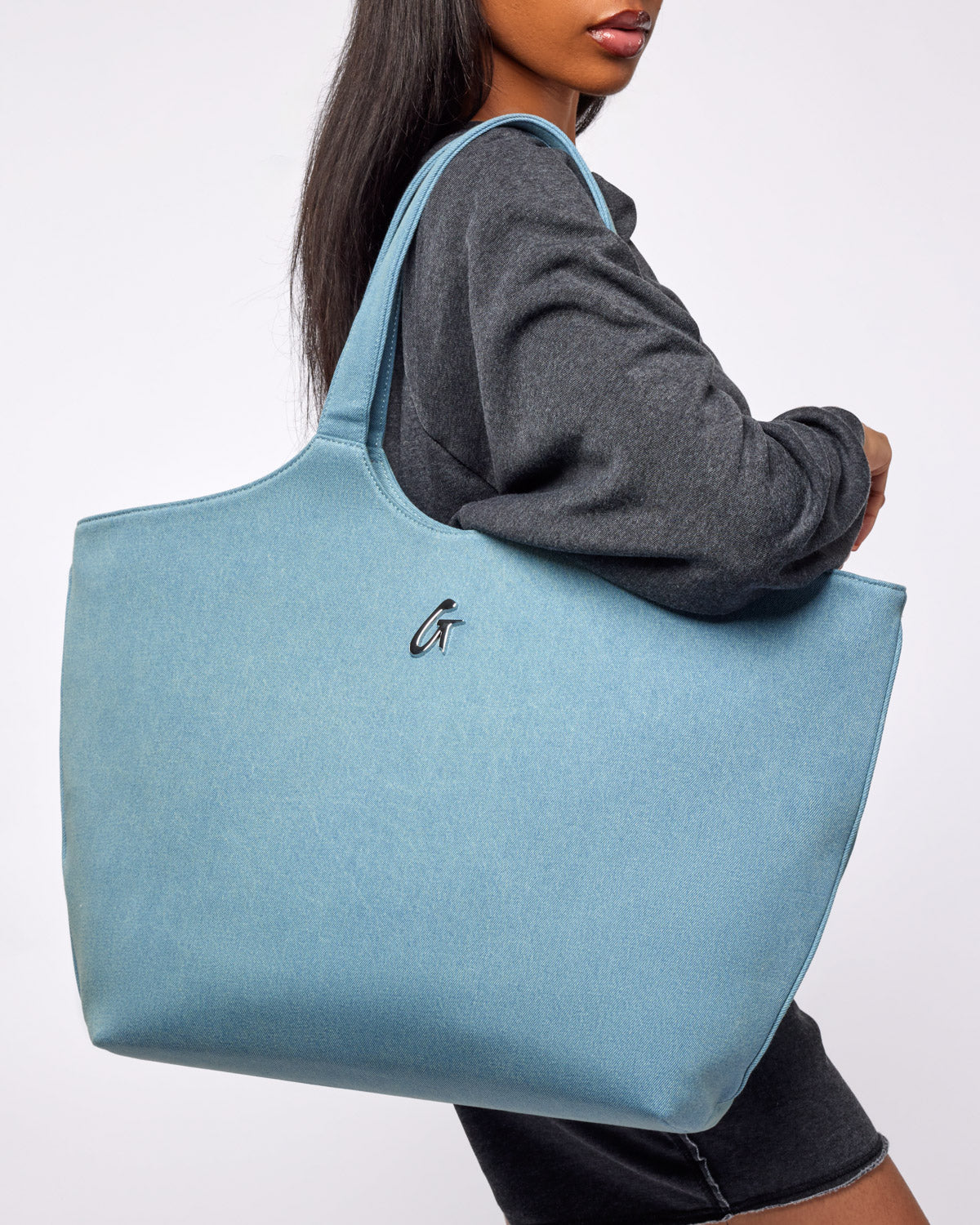 A model showcases a spacious denim silver maxi tote bag, featuring a sleek design and logo detail.